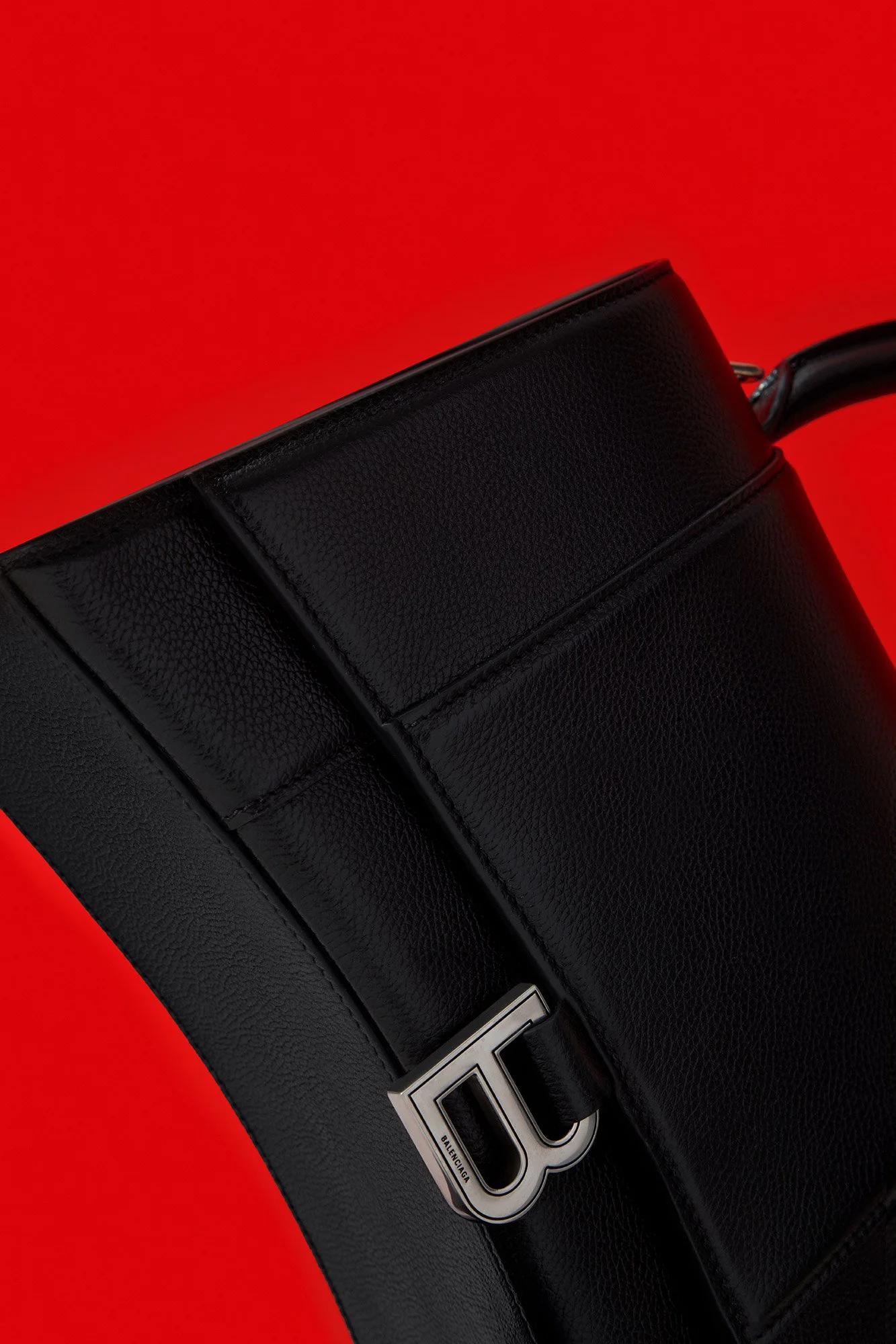 Close-up of a black Balenciaga handbag with a silver logo on a red background.
