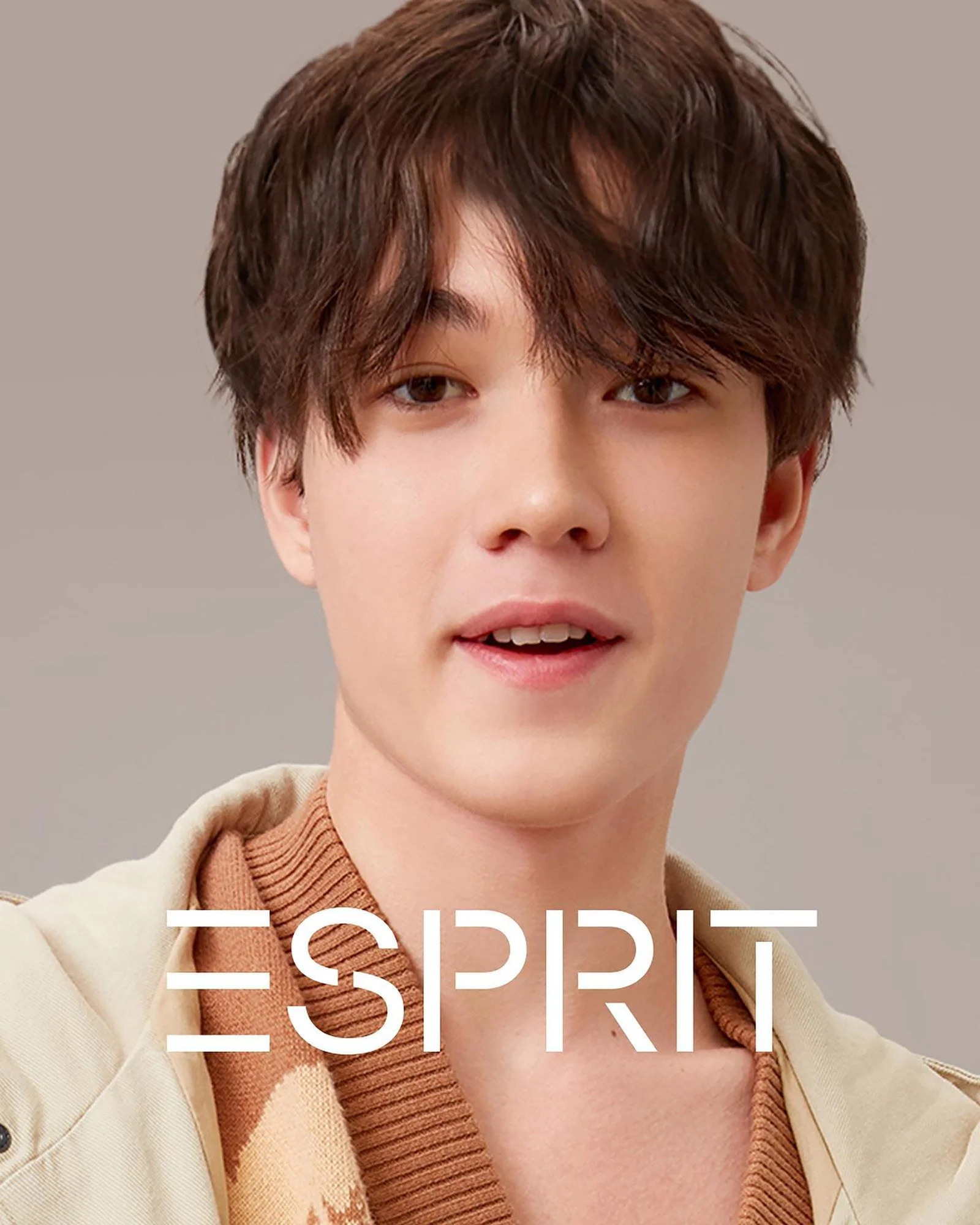 A young man with short brown hair, wearing a beige jacket over a brown patterned shirt, smiling slightly, with the text 'ESPRIT' overlayed at the bottom.