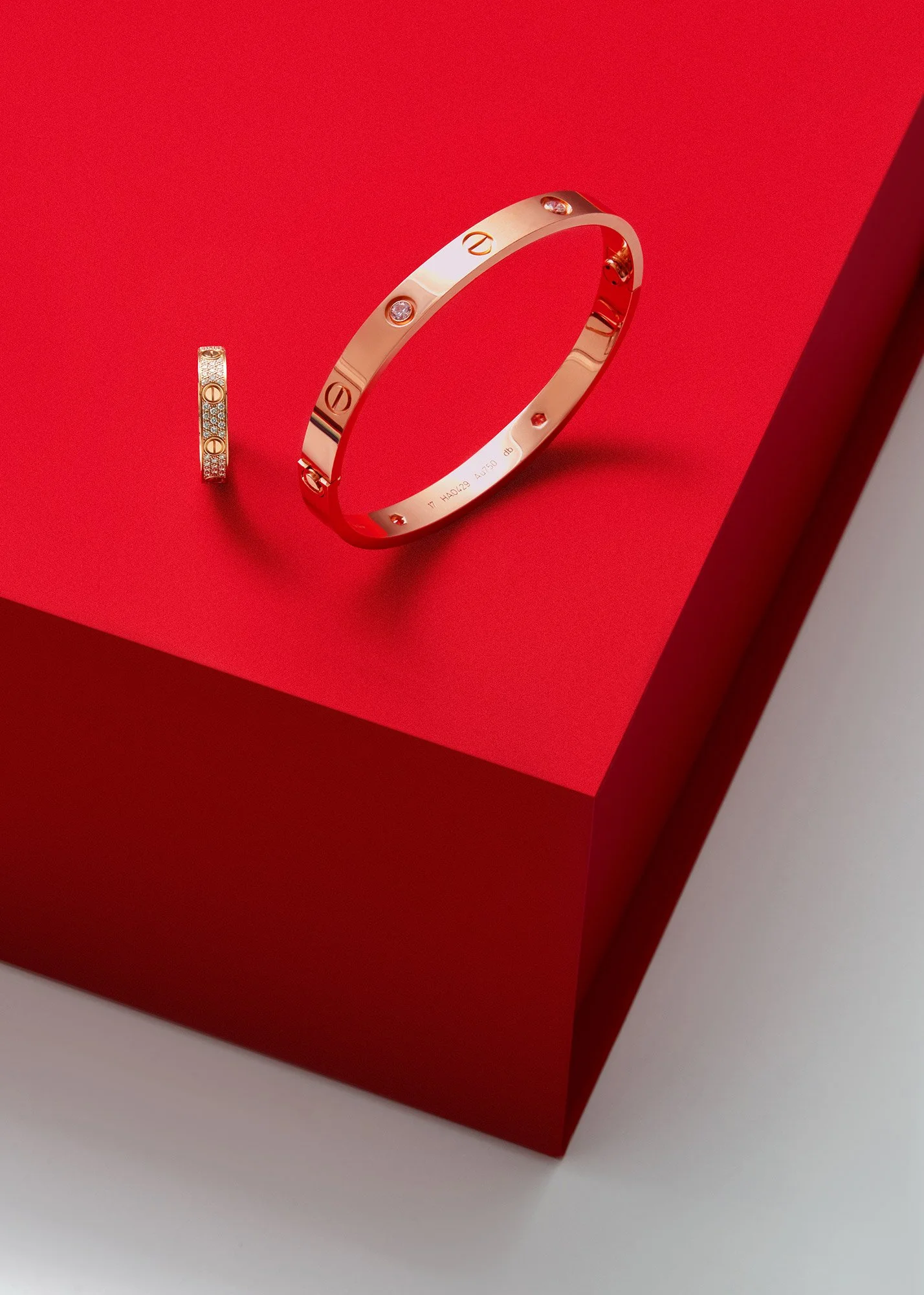 A gold ring with embedded diamonds and a matching gold bracelet with diamond accents, both displayed on a red platform.