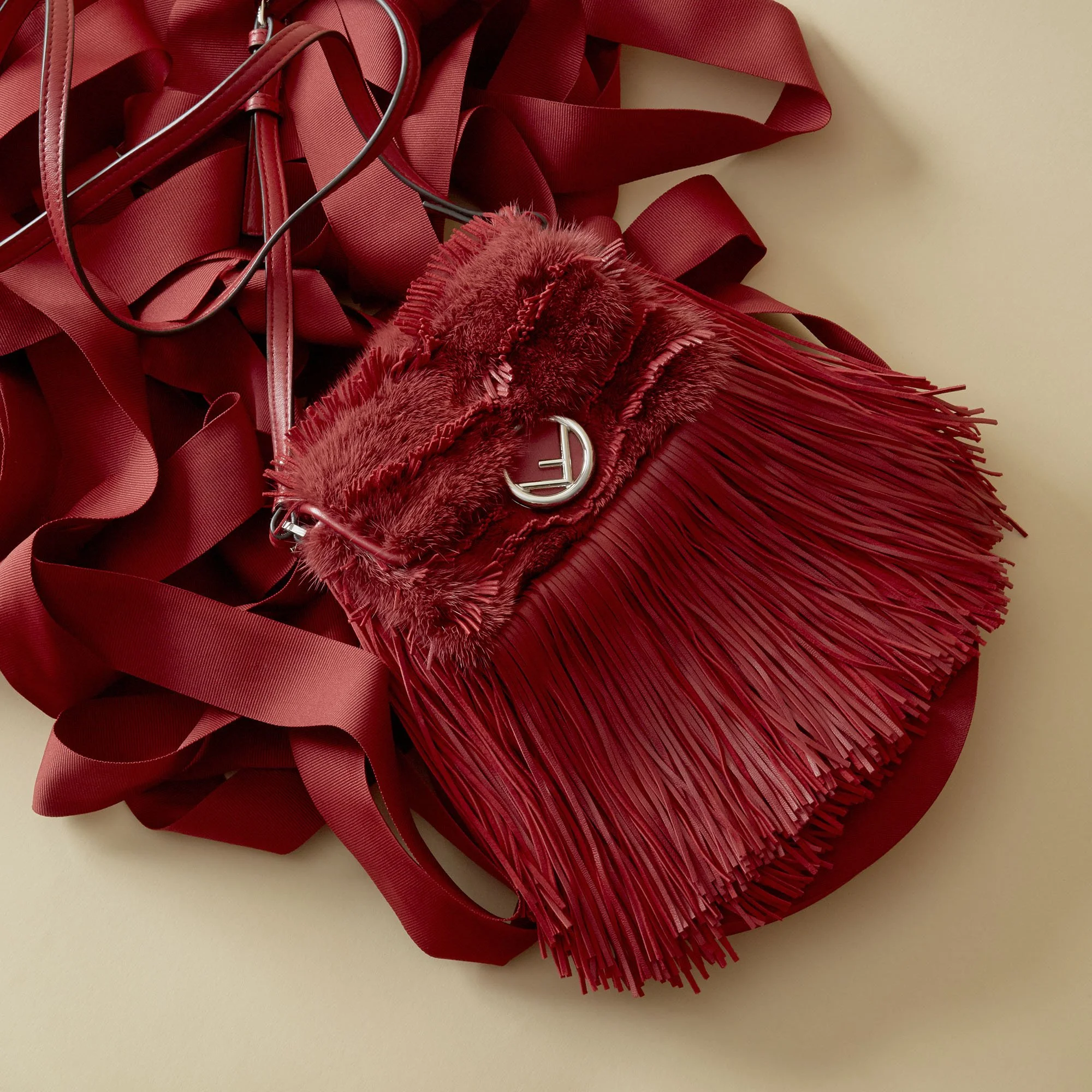 red fringed handbag with fluffy detail and logo, surrounded by red ribbons.