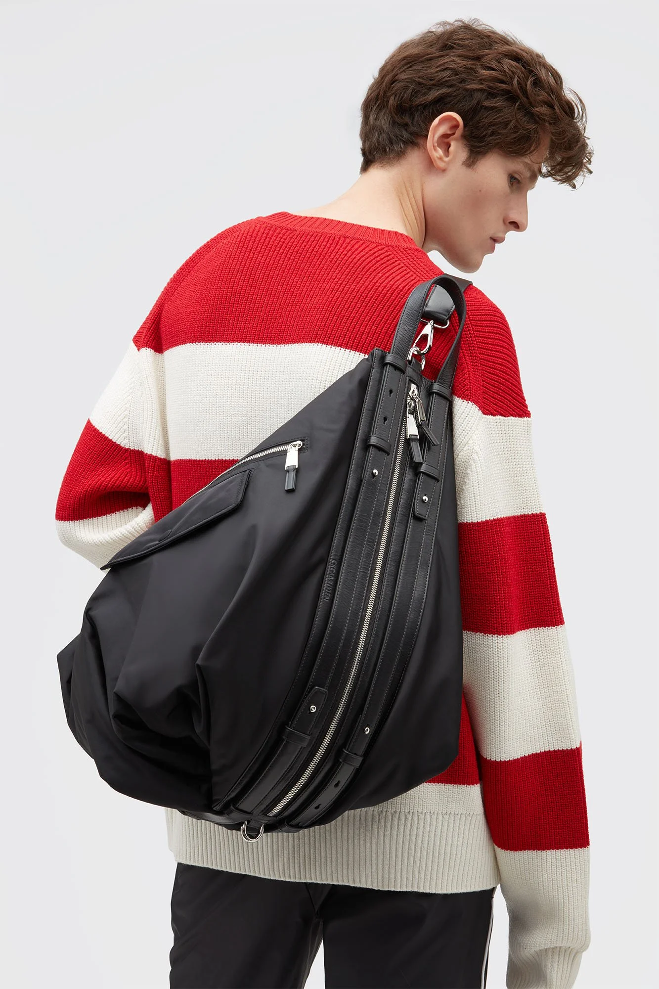 A person with short brown hair wearing a red and white striped sweater and carrying a large black bag over their shoulder.
