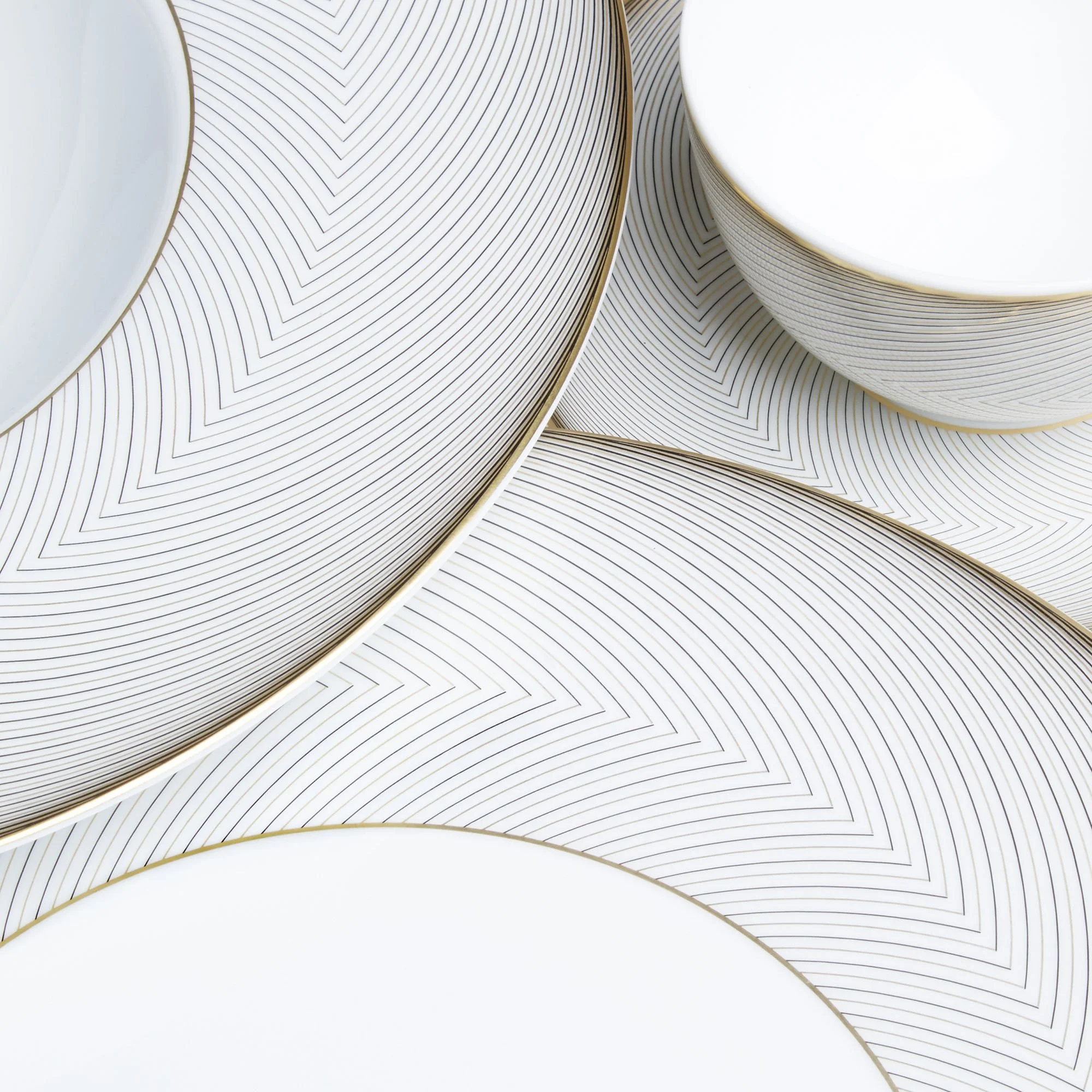 Close-up of white plates with gold rims and geometric black lines, layered on top of each other.