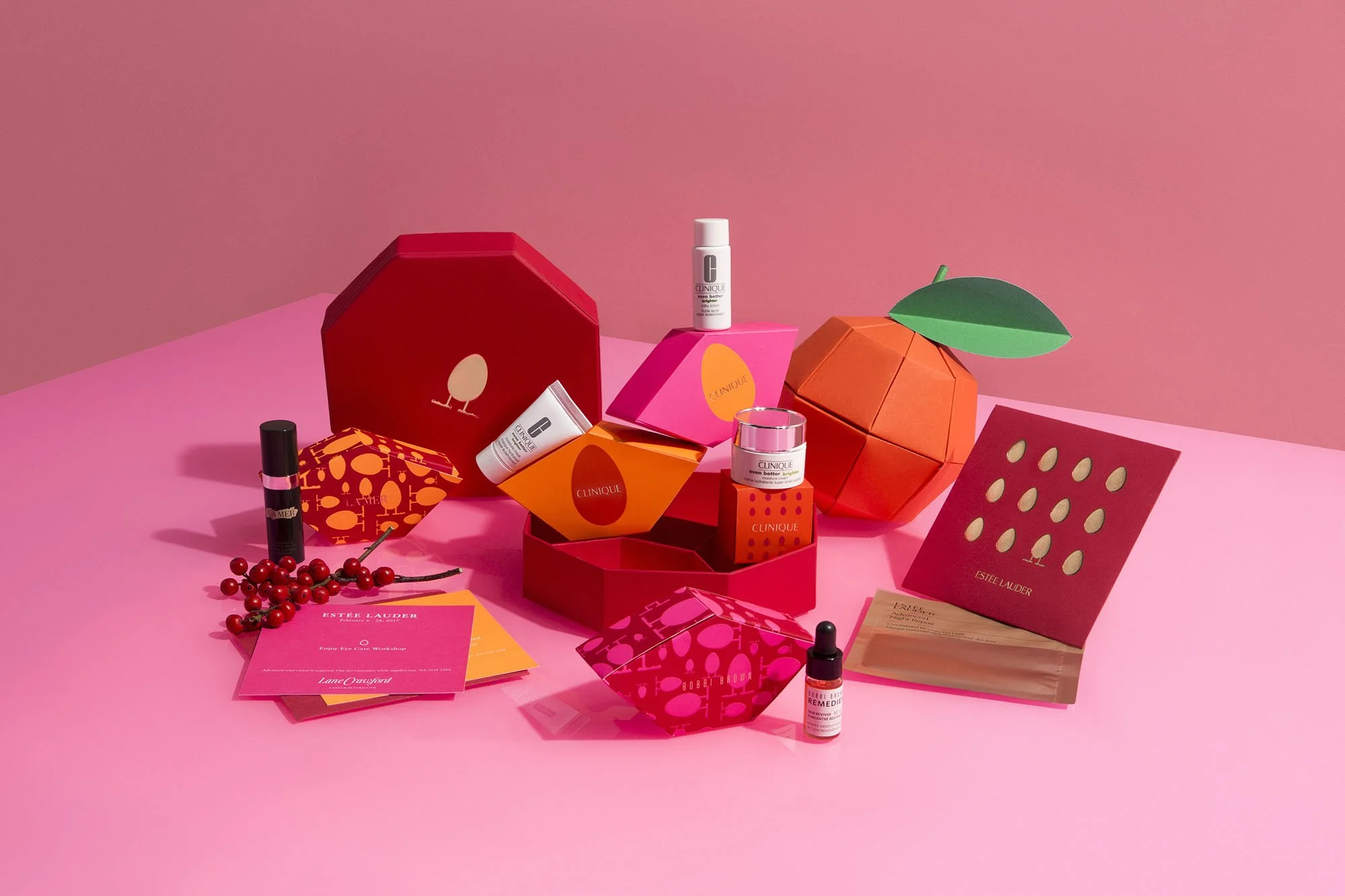 Array of skincare products and gift boxes in pink, red, orange, and green colors on a pink background.