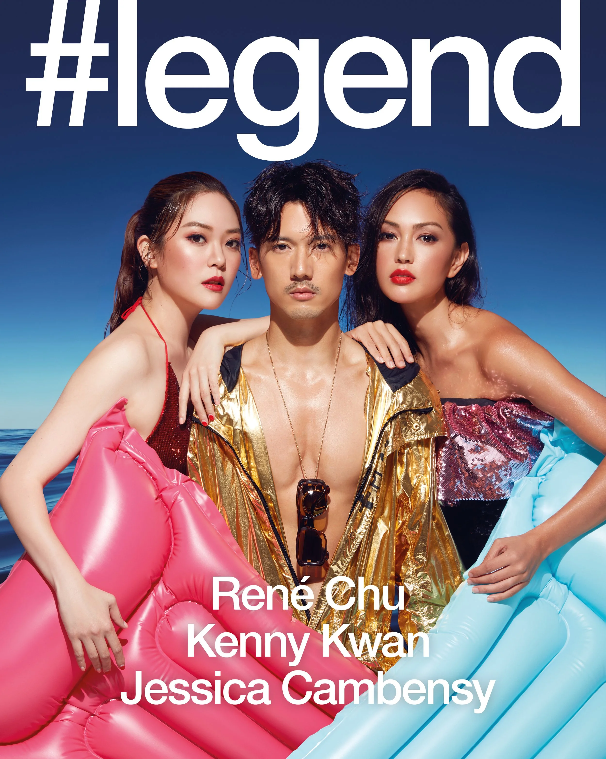 Three individuals are posing by the water during daytime with a clear sky background. They are dressed in colorful, shiny, inflatable outfits and have stylish, bold makeup.