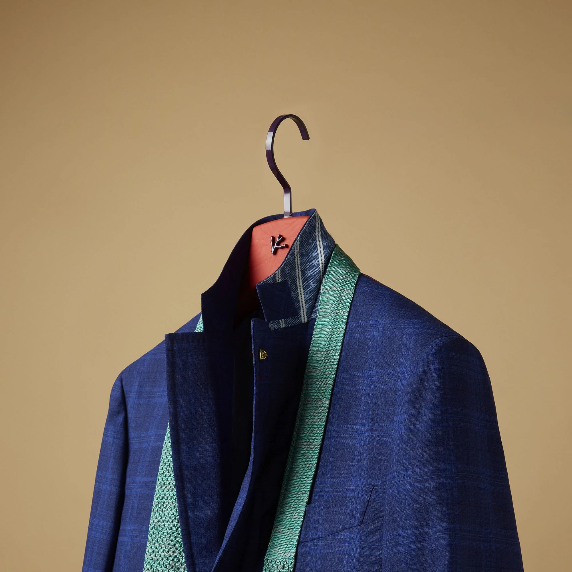 Close-up of a tailored blue suit jacket on a hanger against a plain beige wall.