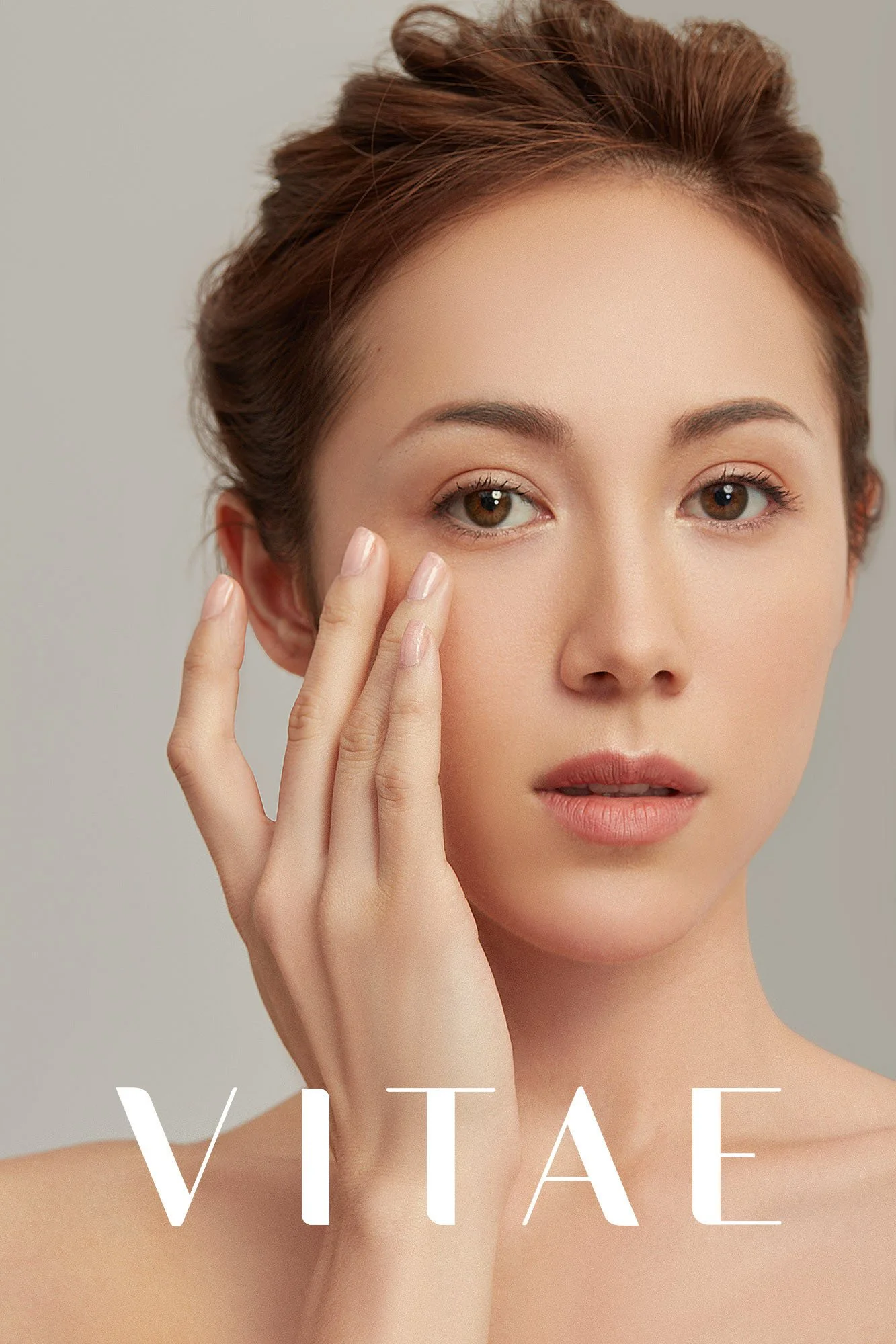 Close-up of a young woman with natural makeup, touching her face with her fingers, and the word 'VITAE' overlaid at the bottom.