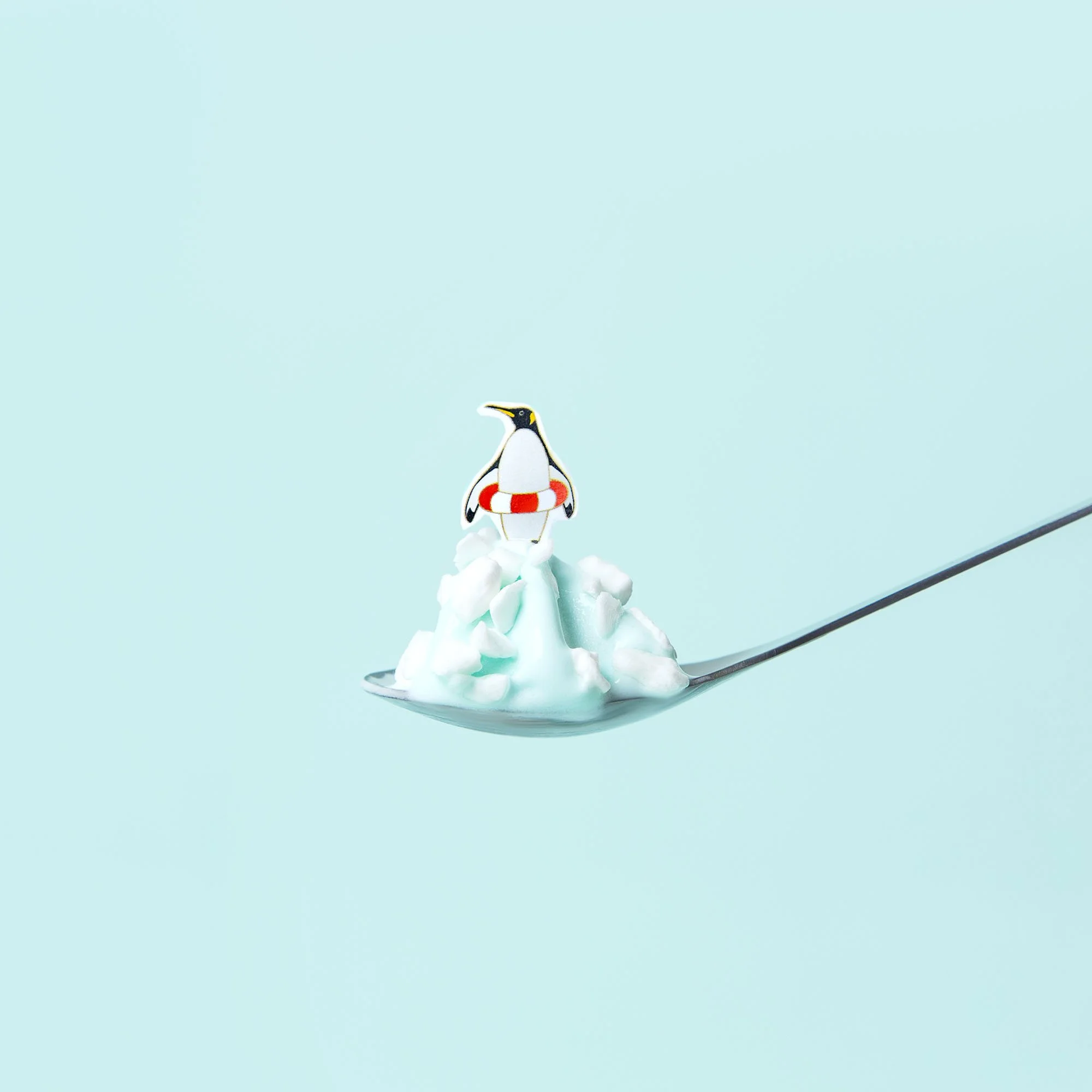 A spoonful of white creamy substance with a cartoon penguin figure on top, set against a light blue background.