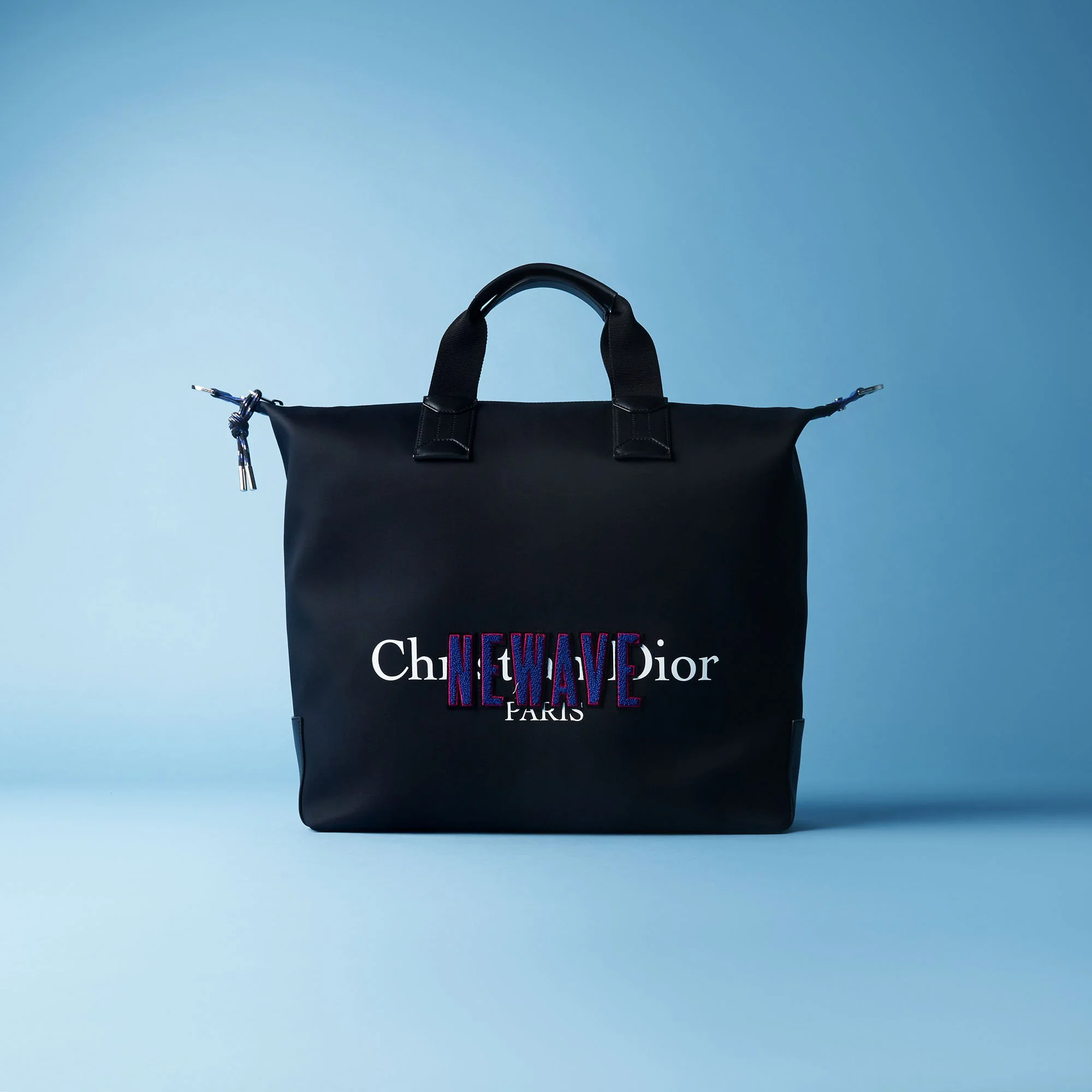 Black designer tote bag with multicolored embroidered text that reads 'CHANEL' and 'PARIS' on a blue background.