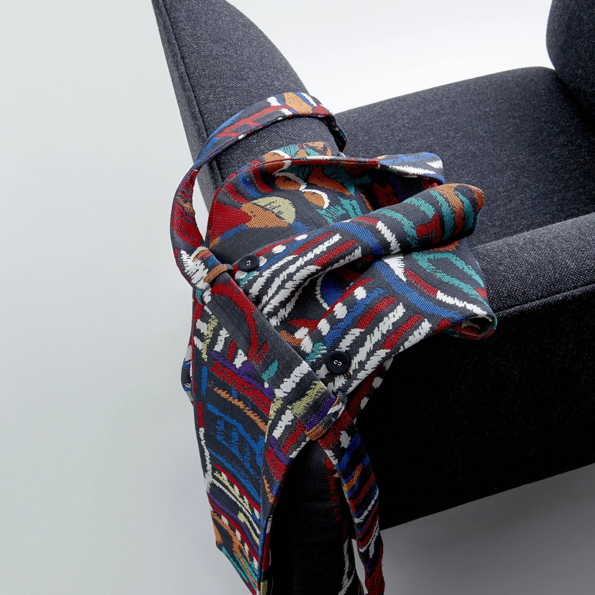 A colorful, patterned fabric scarf draped over the armrest of a dark gray upholstered chair.
