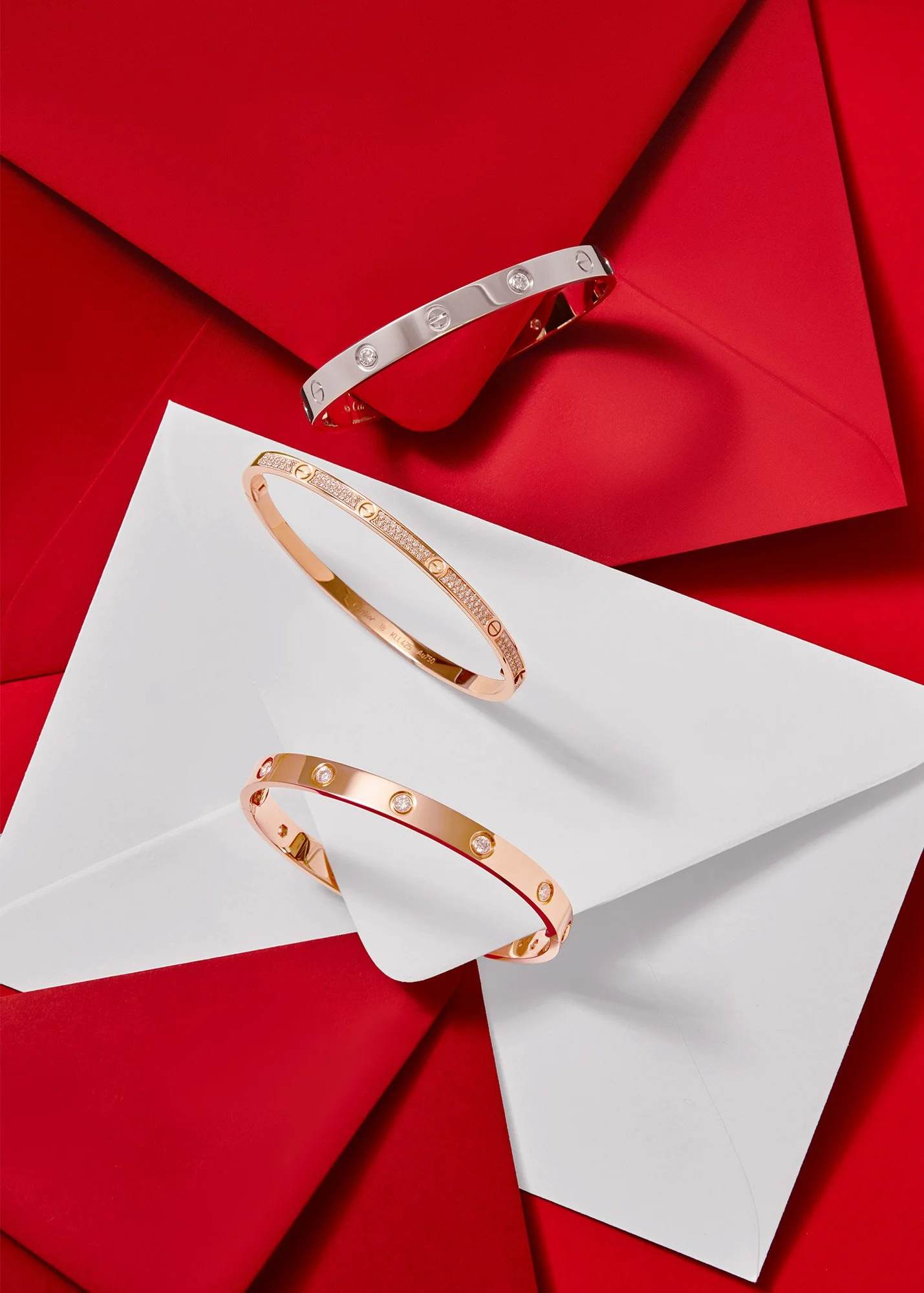 Three designer bracelets displayed on a white envelope and red background.