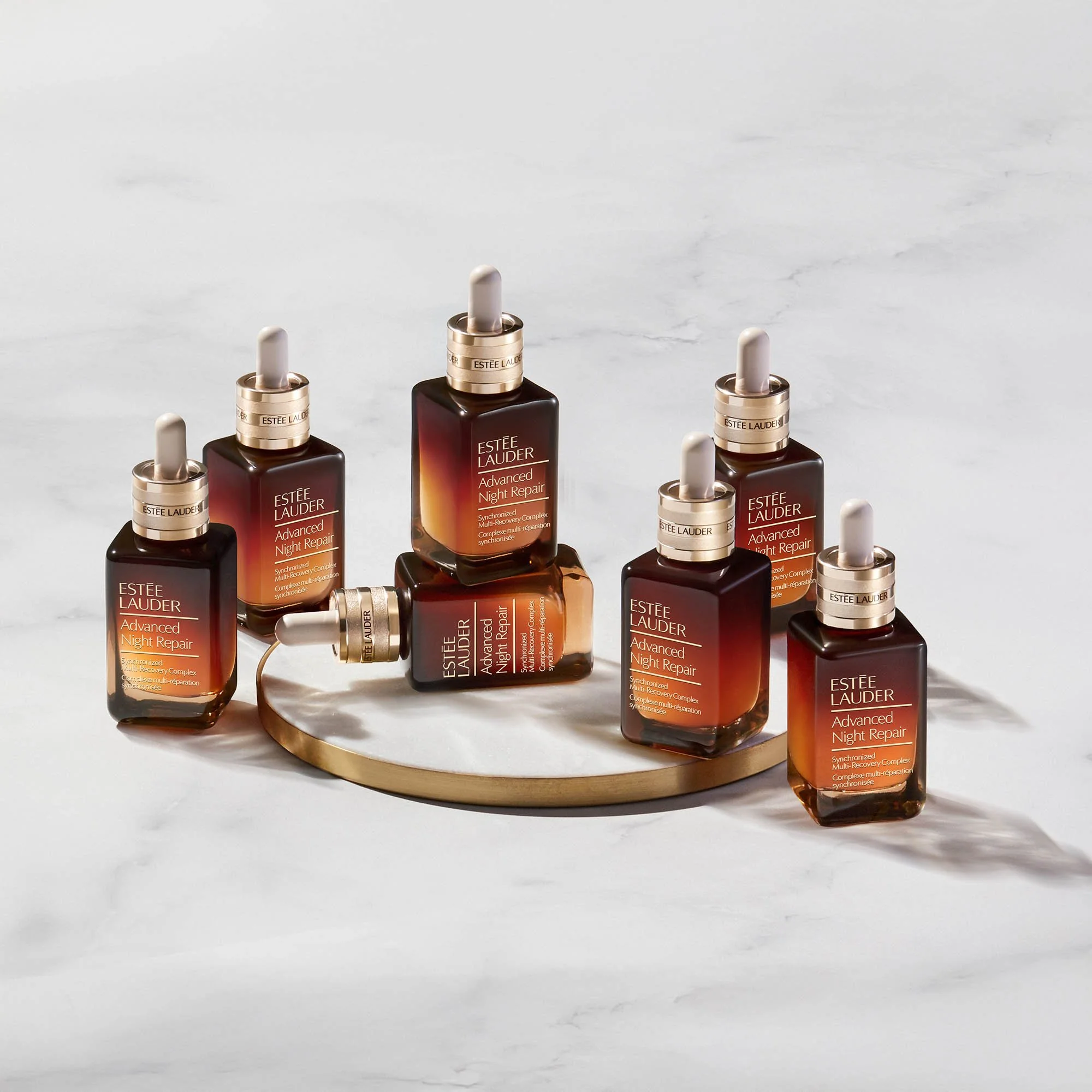 Multiple bottles of Estée Lauder Advanced Night Repair serum displayed on a white marble surface with a round tray.