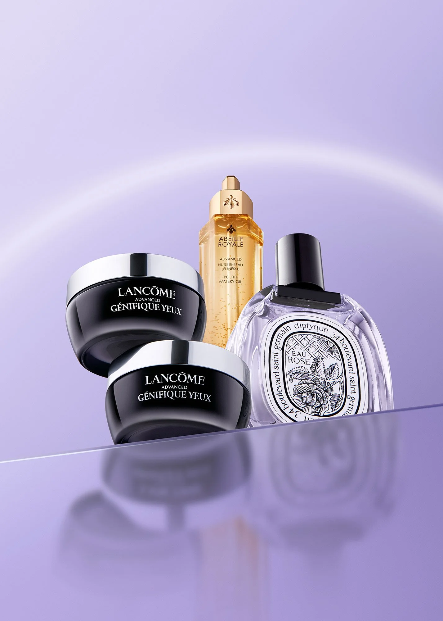 Beauty products on purple surface, including Lancôme eye cream, Dior skincare oil, and Diptyque perfume with a purple background.