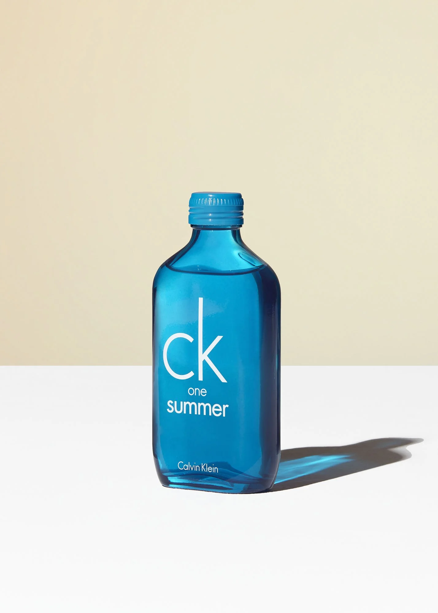 A blue Calvin Klein CK One Summer perfume bottle on a white surface with a two-tone background.