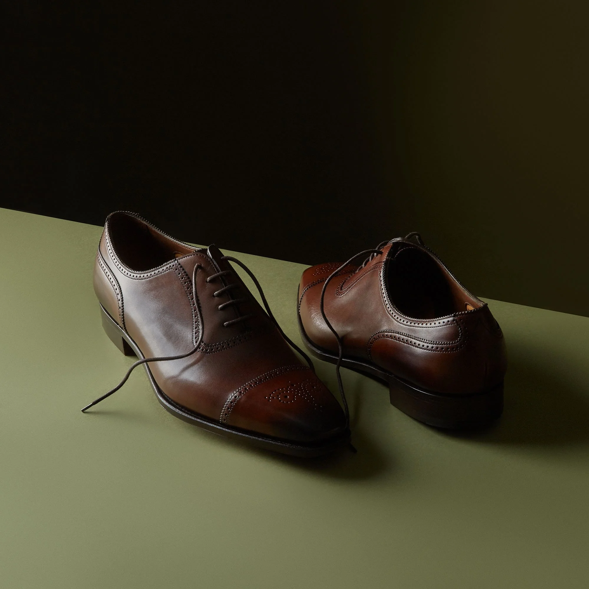Pair of brown leather dress shoes on a two-tone background.