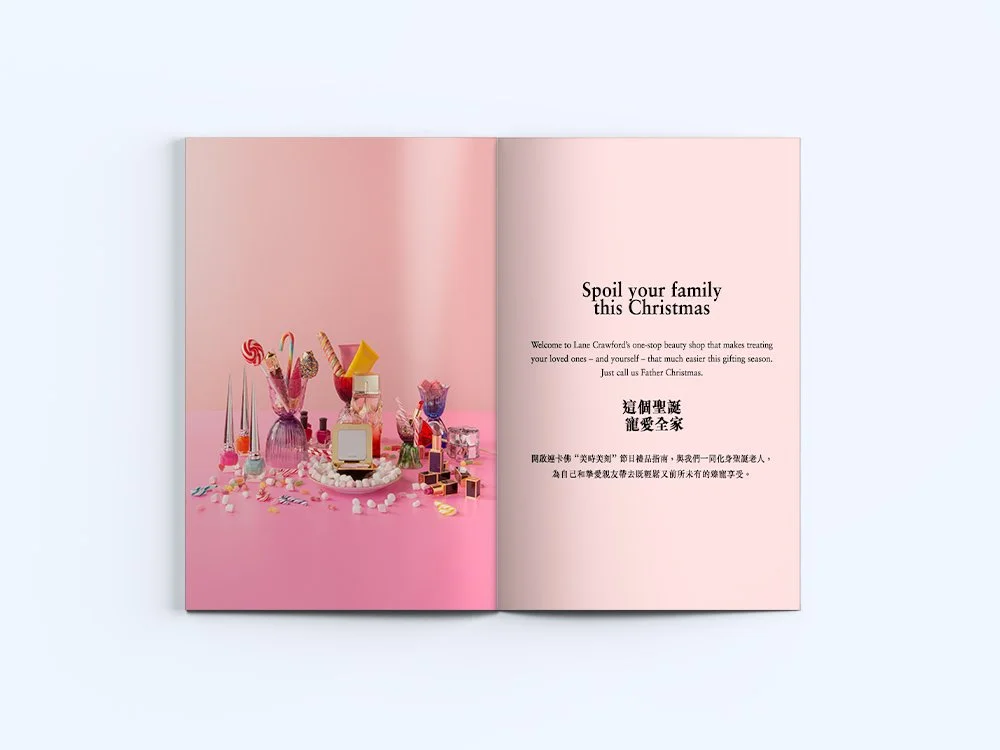 An open book with a pink background on each page. The left page has a display of various makeup products and cosmetics arranged with pink and white decorations. The right page features the text "Spoil your family this Christmas" and a paragraph about