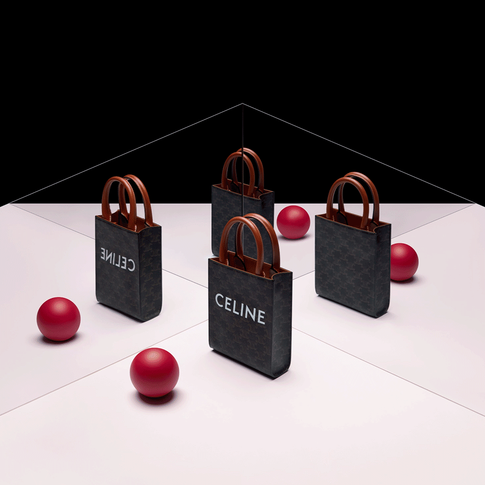 Three black Céline shopping bags with brown handles are arranged on a pink and black mirrored surface. Red balls are placed around the bags, with one ball also reflected in the mirror.