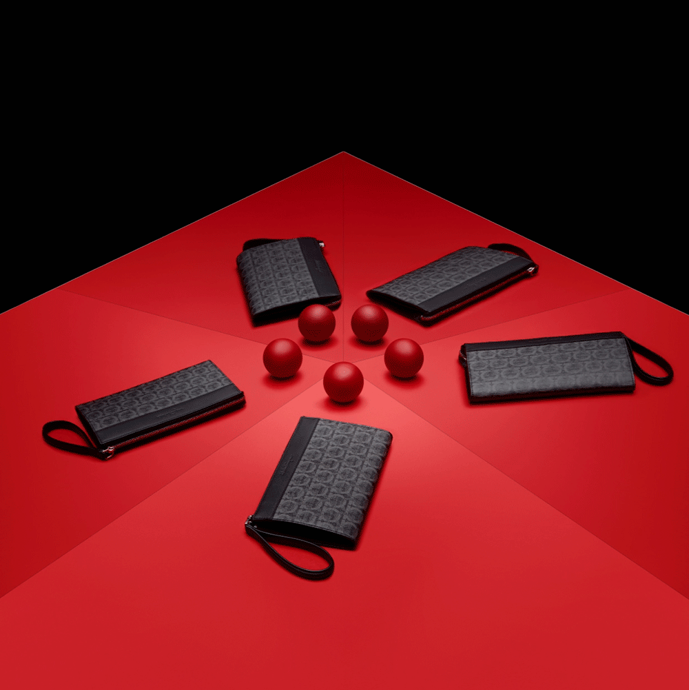 Five black zippered pouches with wrist straps arranged in a circle on a red surface, with red spherical objects in the center, black background.