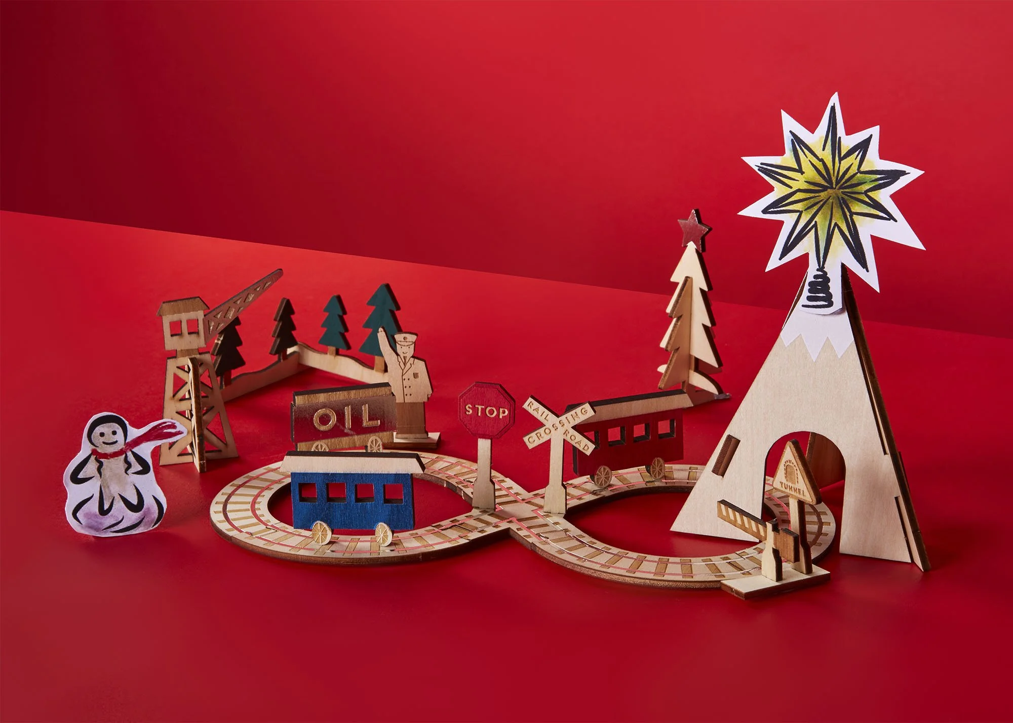 Colorful miniature train set with wooden trees, a coal car, a stop sign, crossing sign, and a mountain with a star on top, set on a red background.
