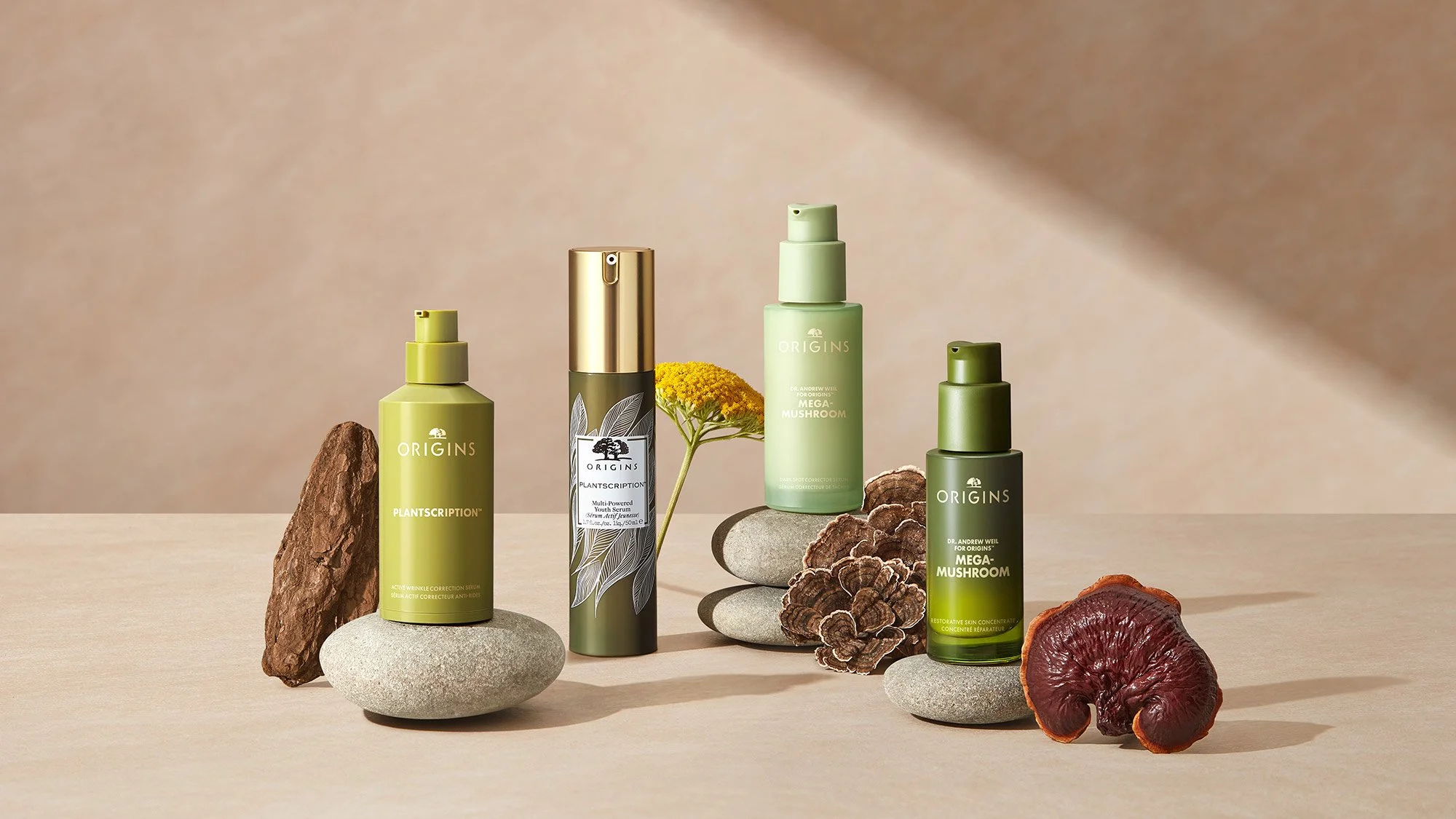 Four skincare products from Origins line, surrounded by rocks, mushrooms, and a flower on a light wooden surface.