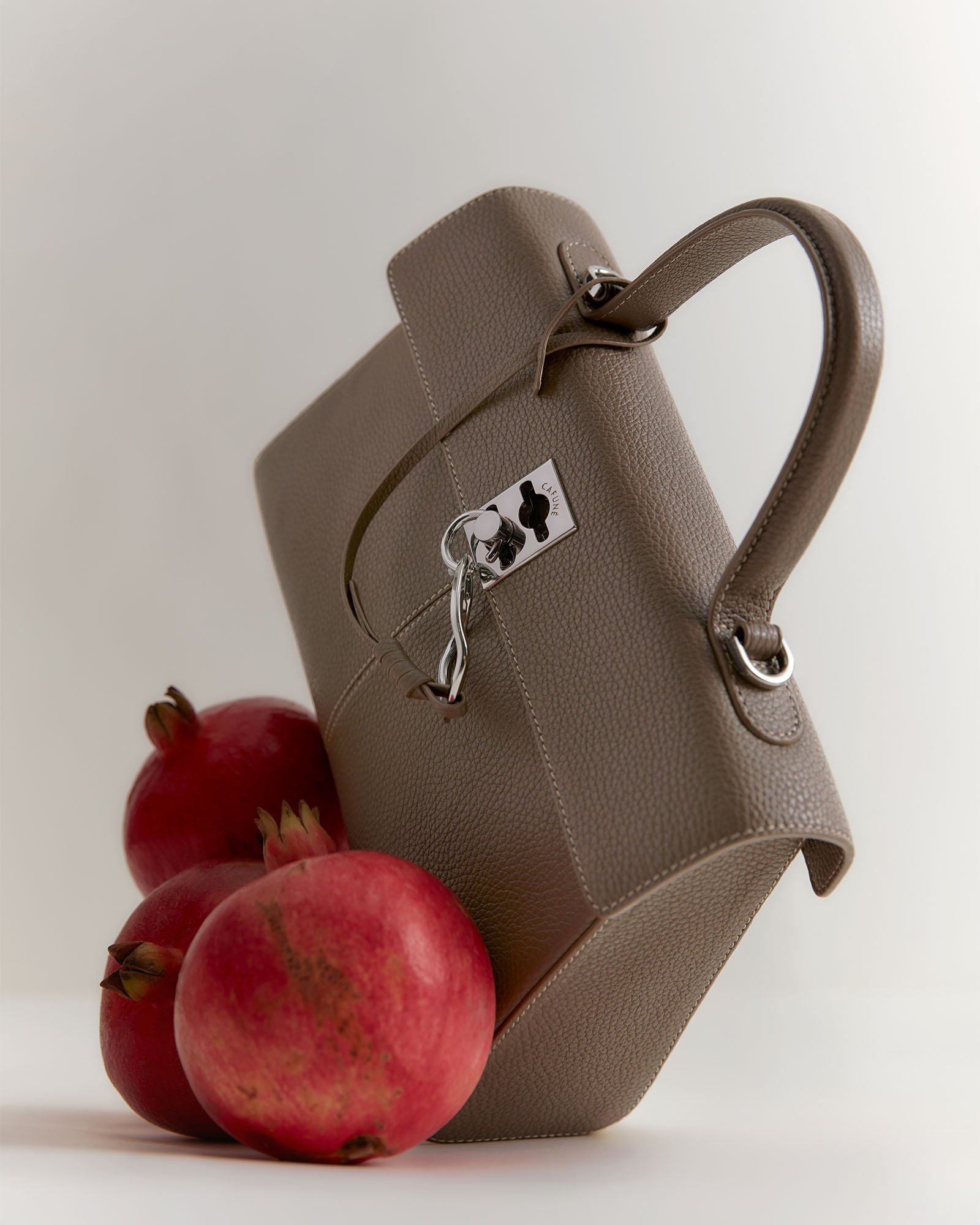 A close-up of three pomegranates next to a beige designer handbag with a textured surface and silver hardware