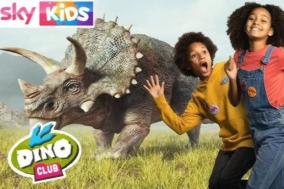 Two children, a boy and a girl, are posing excitedly in front of a realistic-looking dinosaur model with a grassy background. The image features Sky Kids and Dino Club logos.