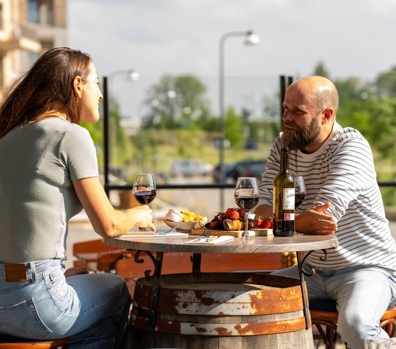 Een man en vrouw zitten buiten aan een tafel, drinken rode wijn, met eten op tafel.