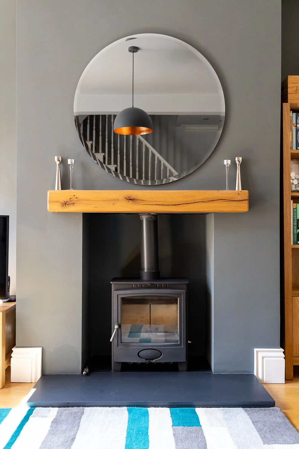 Modern living room with a black wood-burning stove, wooden mantel, round mirror, and contemporary decor.