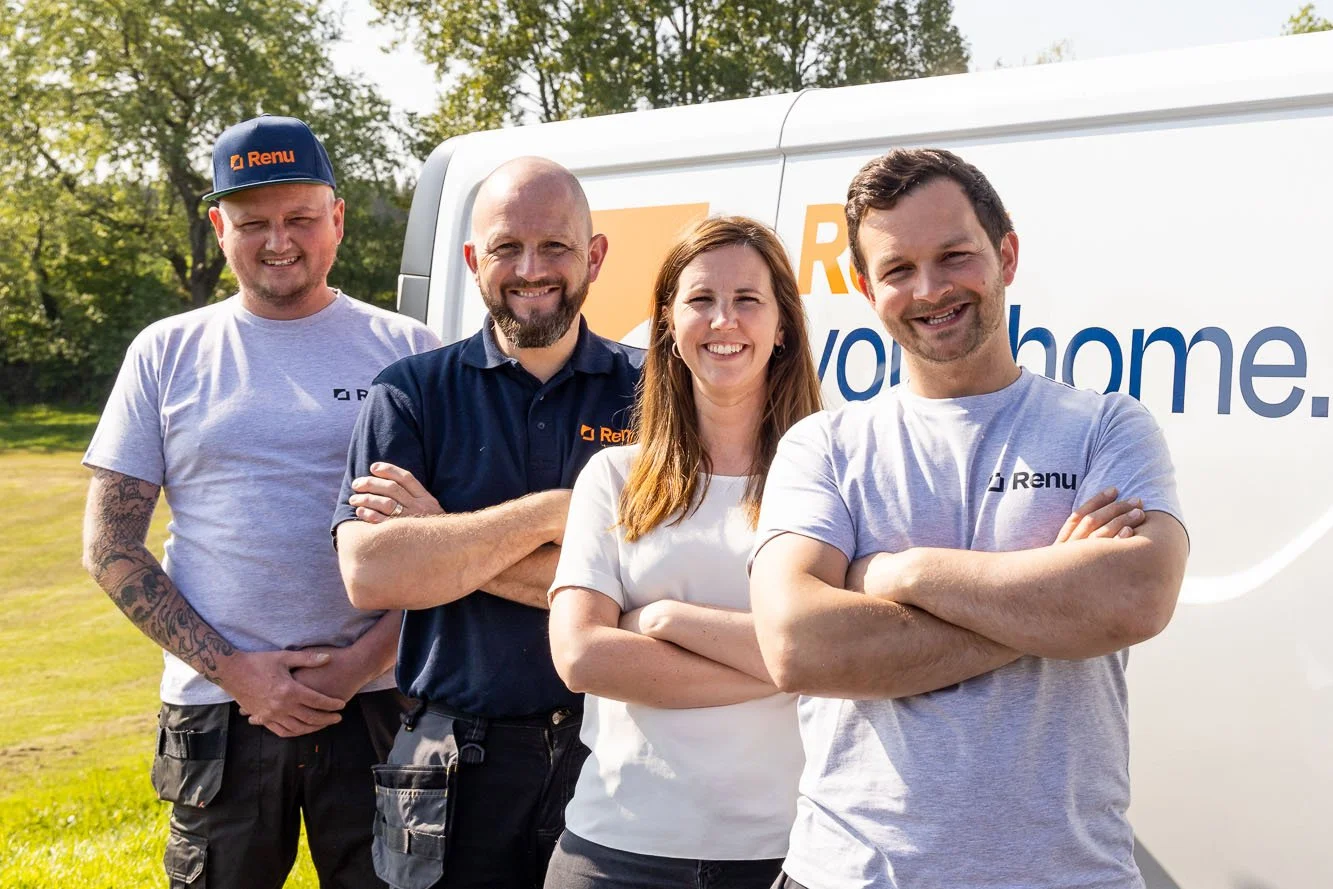Group of four people smiling, standing in front of a white van with "Renu" logo, in an outdoor setting with trees.