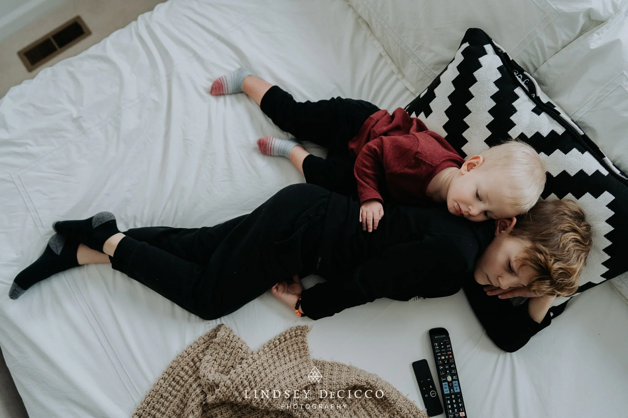 Two brothers cuddle together on a cozy bed during an at-home family film session in Mishawaka, Indiana. Captured by Lindsey DeCicco Photography
