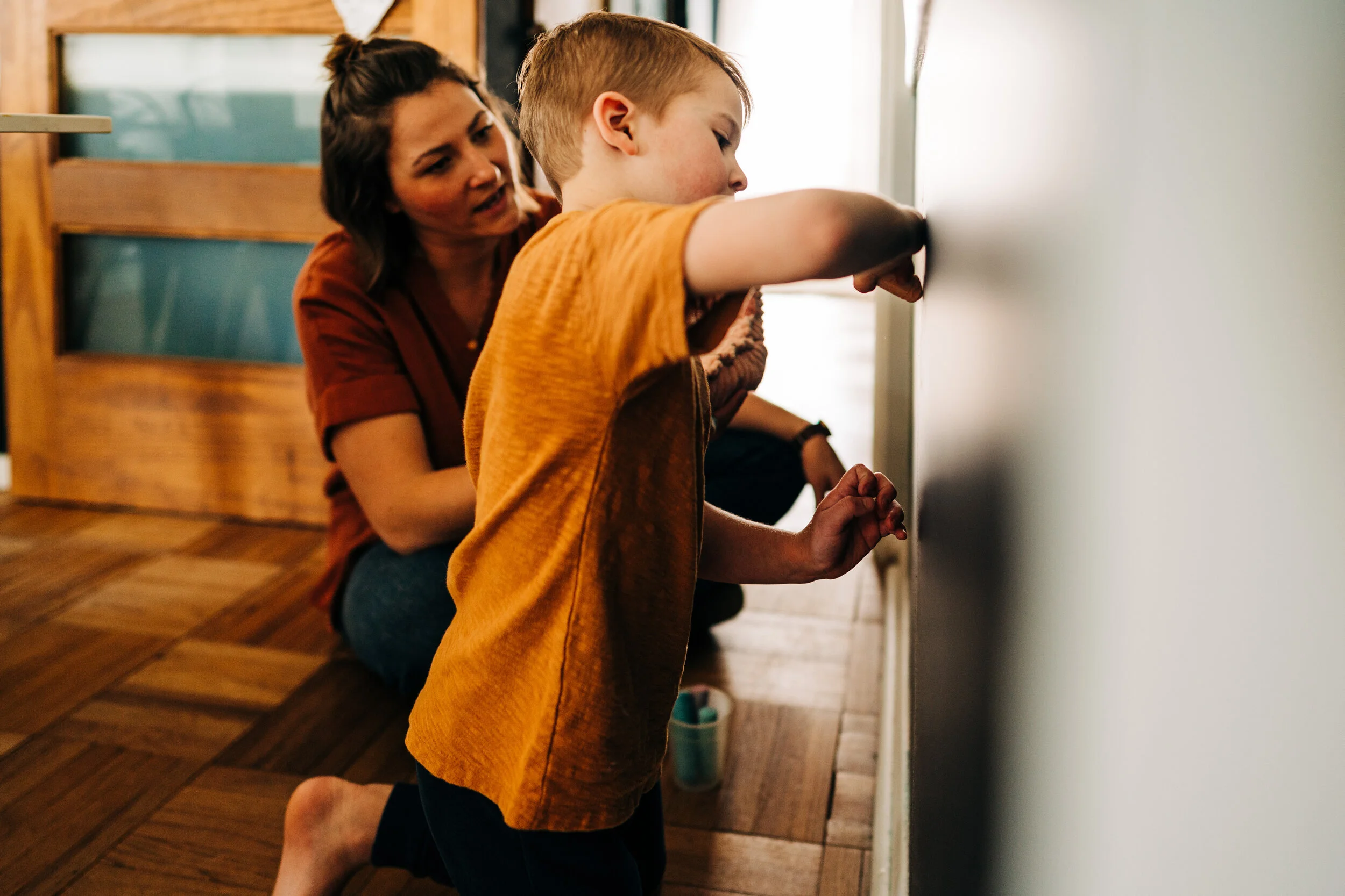 A heartwarming image of a mother guiding her child as he writes on the wall, a moment of playful creativity and family connection.