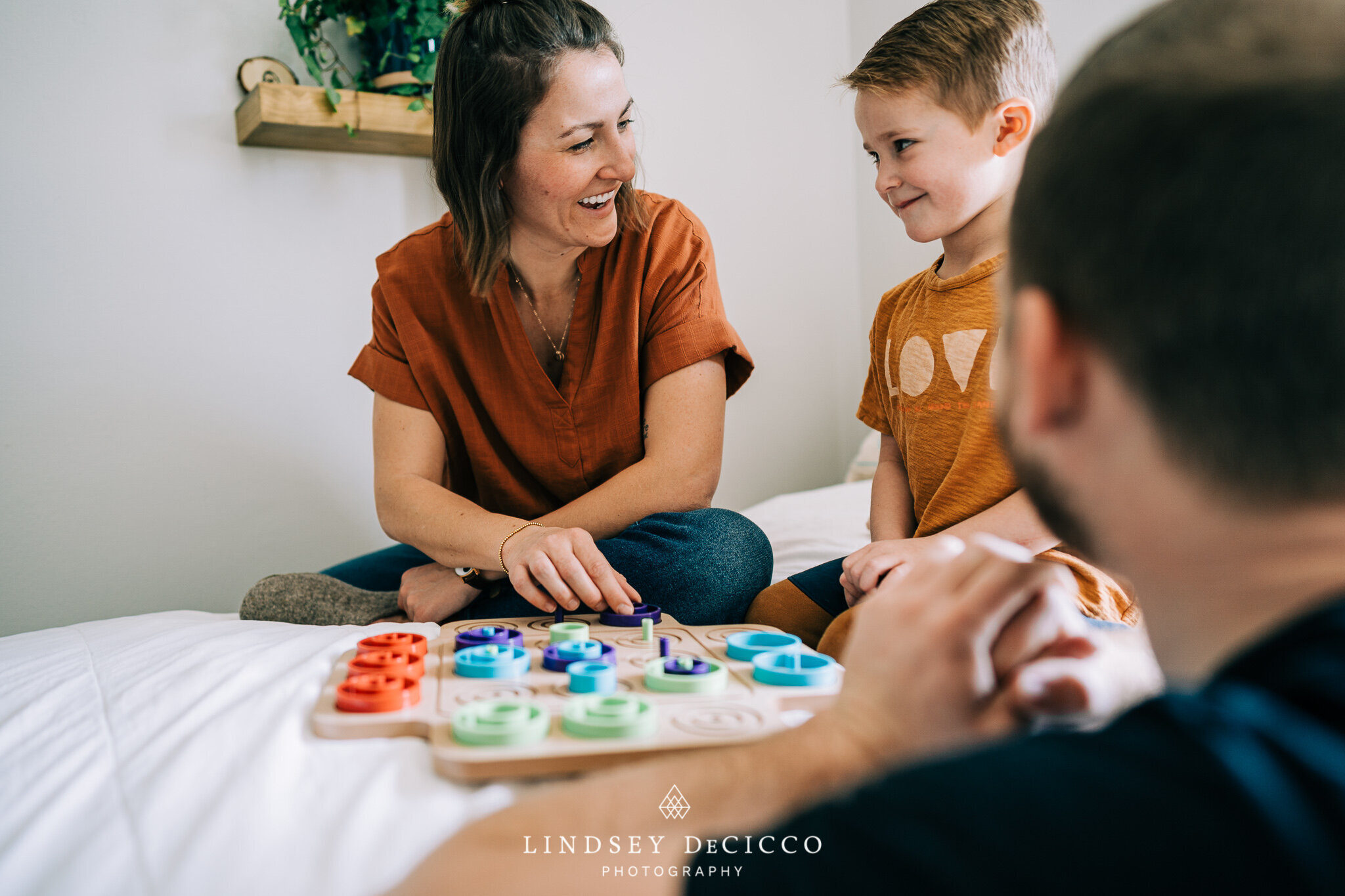 A mother and son smile while playing a colorful puzzle game, with the father joining in the background.