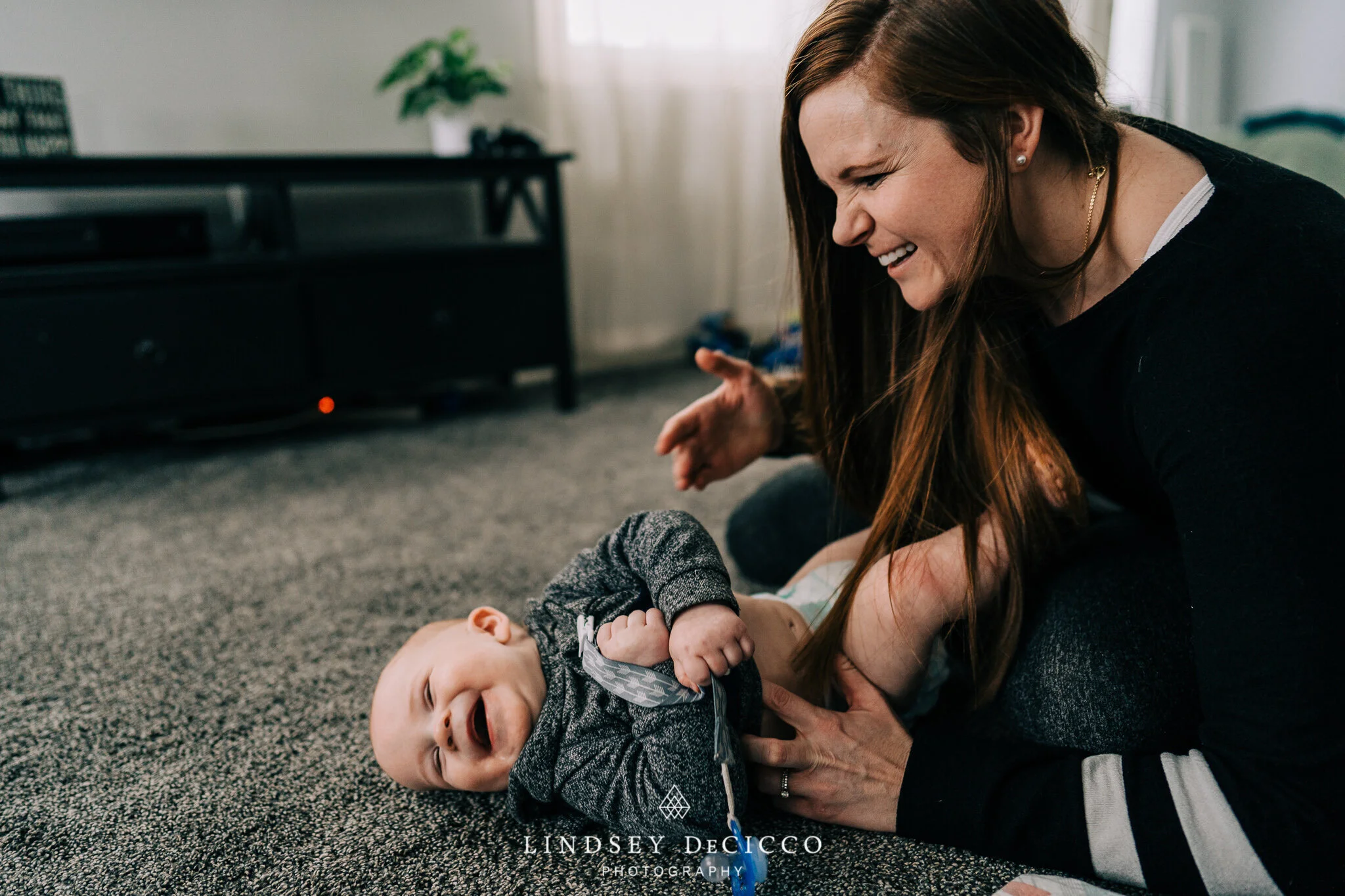 Candid moment of a mother tickling her laughing six-month-old on the carpet—authentic, in-home lifestyle photography for a Grow With Me baby milestone video in Northern Indiana.
