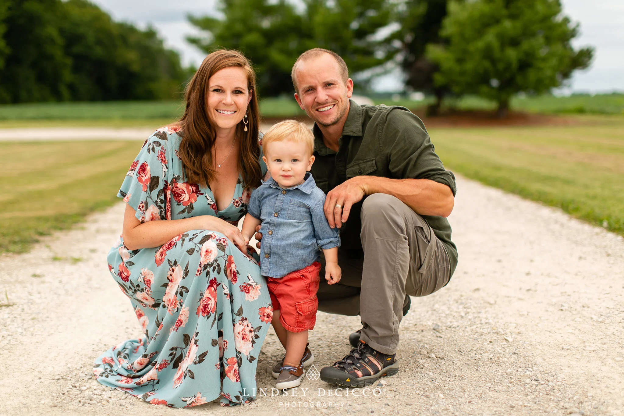 Parents kneel beside their toddler son on a gravel road in rural Mishawaka, smiling together during a relaxed outdoor family session.