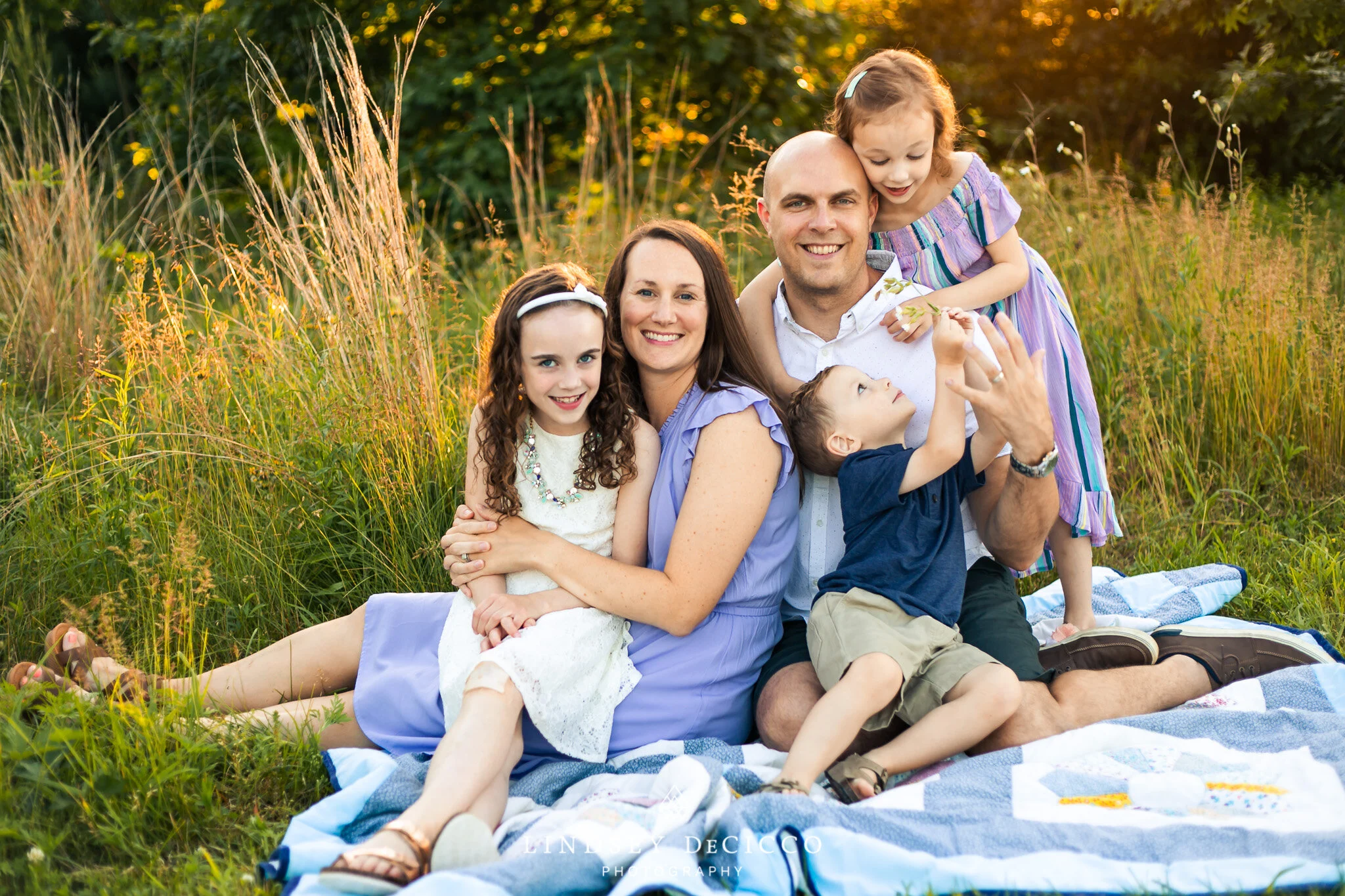 The family of five captured in a relaxed, joyful moment as they pose together on a blanket, basking in the warm evening light.