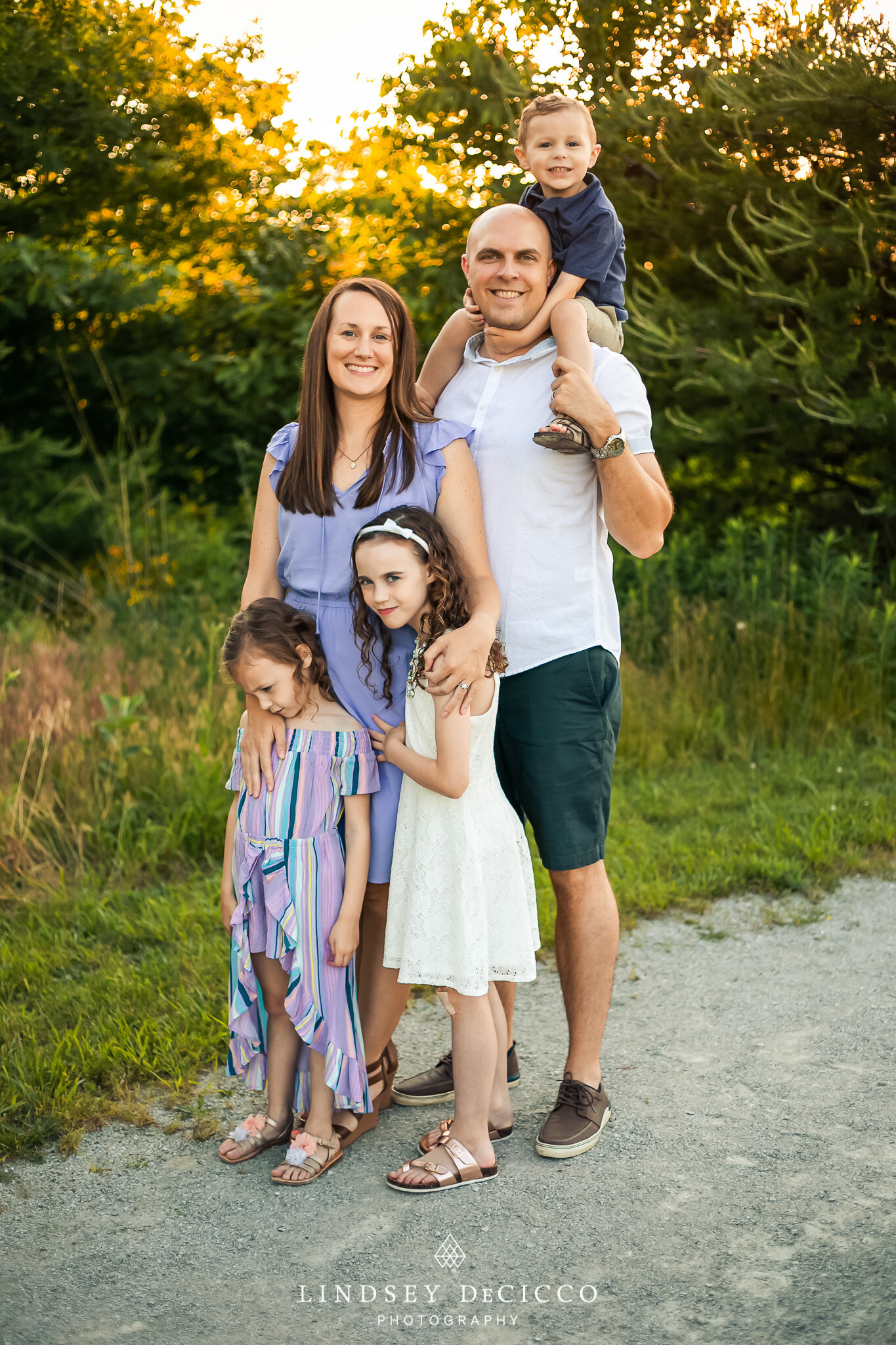 A joyful family moment, with the parents and three children smiling and posing together during their family photo session in a scenic park at sunset.