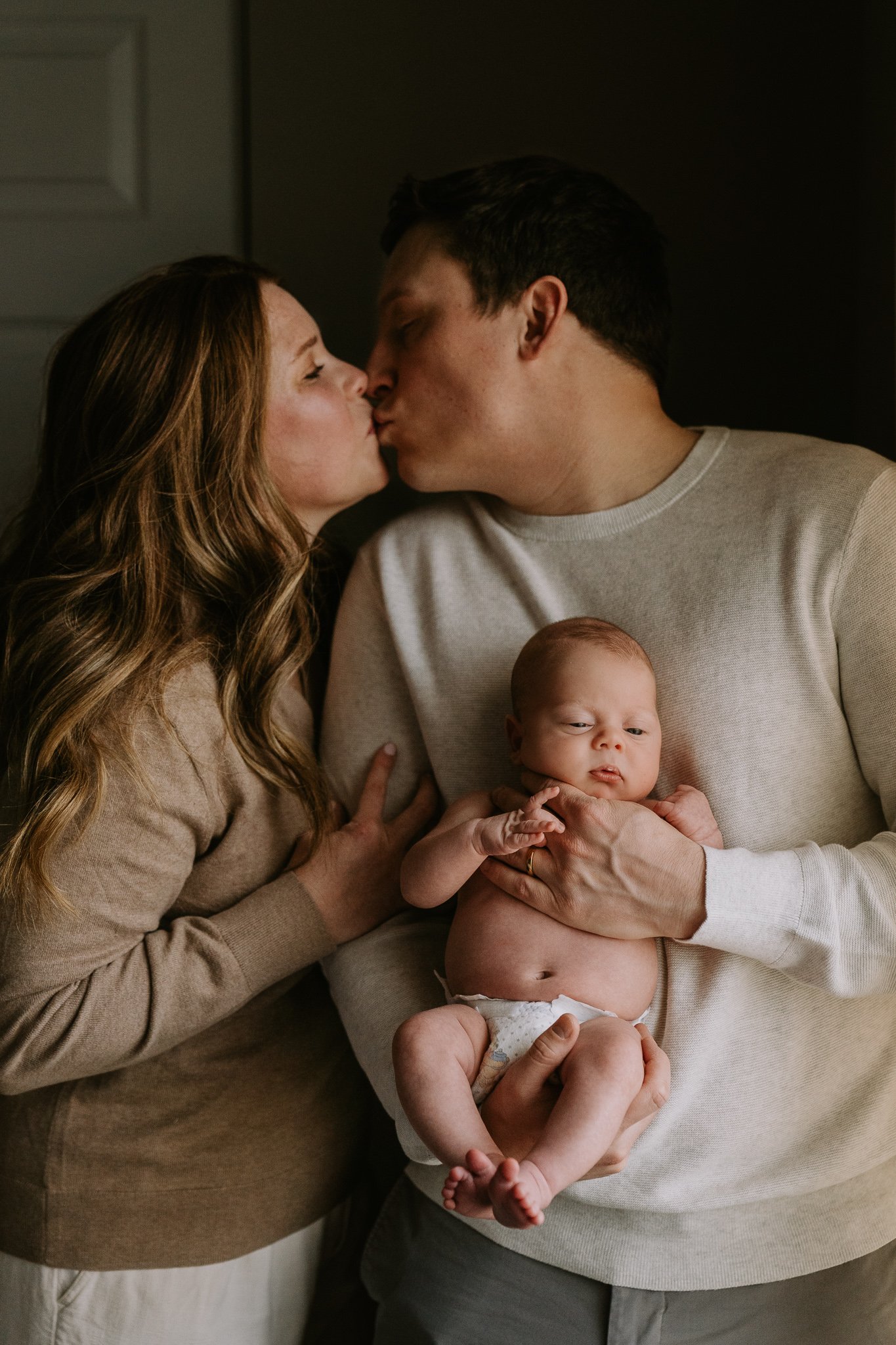 parents kiss over newborn