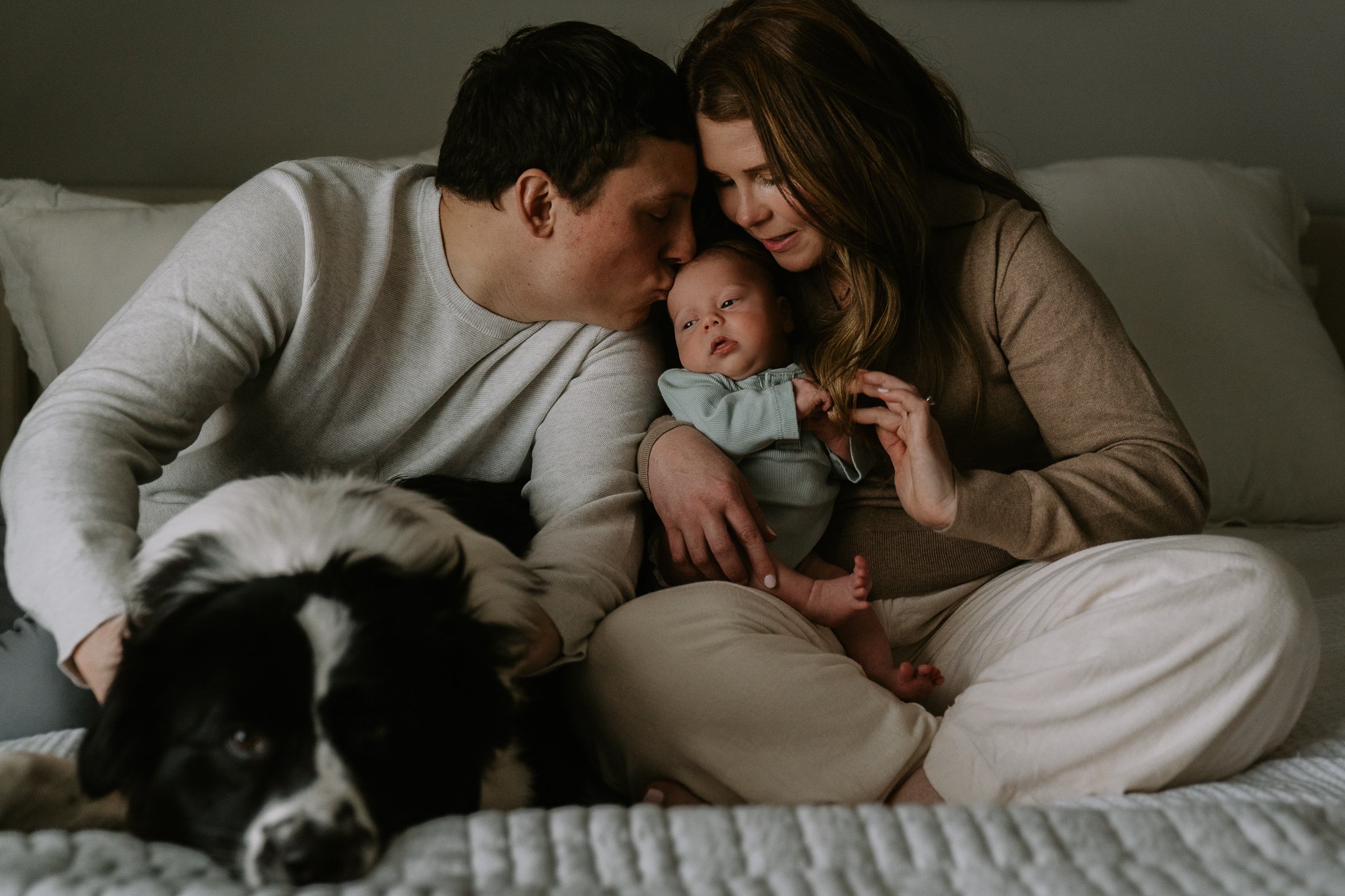 a mom and dad snuggle with their newborn and their dog