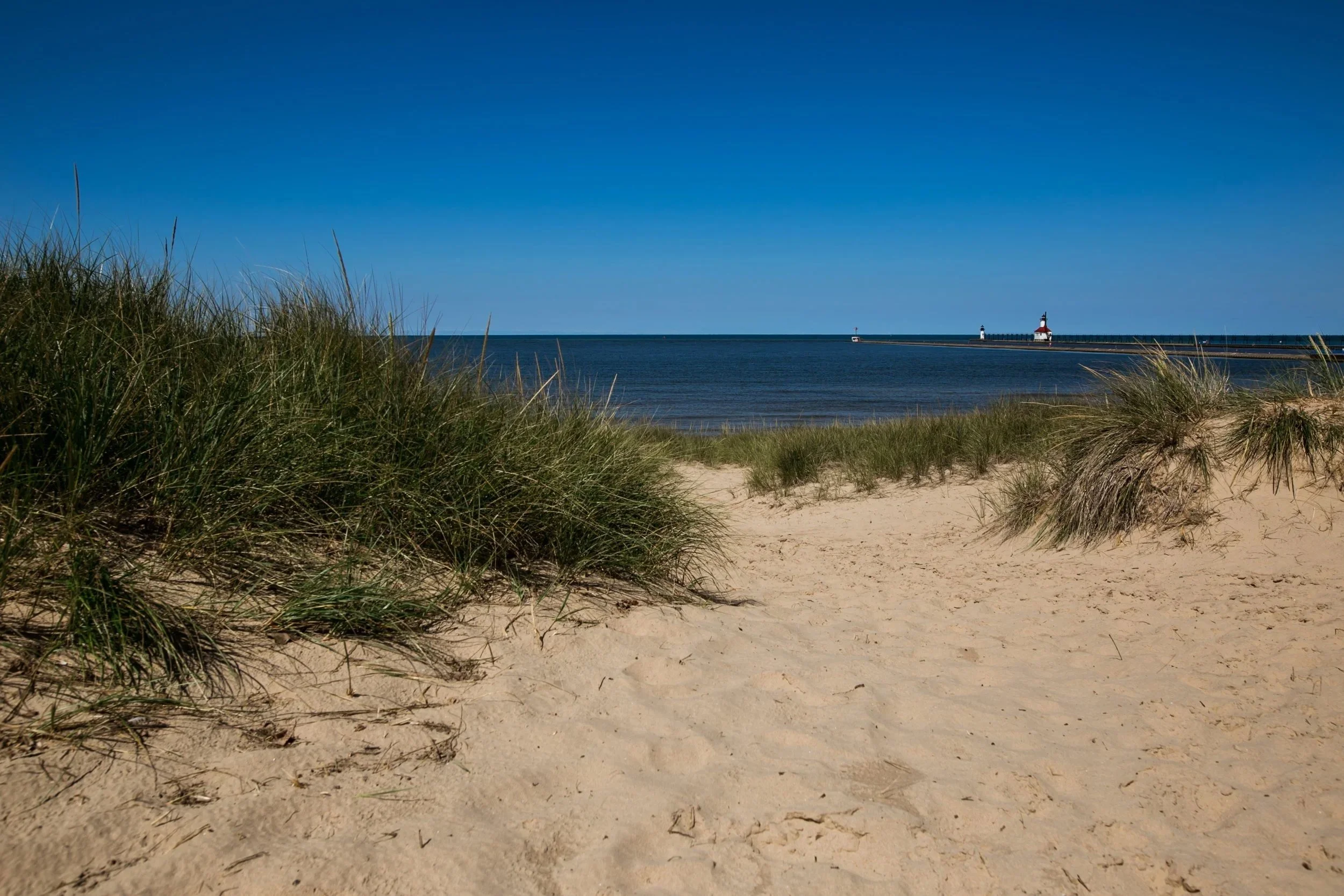 Vibrant blue skies and deep blue waters of Silver Beach in St. Joseph, Michigan, from the dunes toward the historic lighthouse.