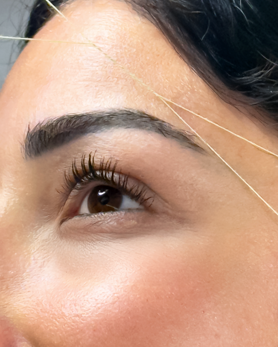 Primo piano di un occhio con un filo per la depilazione delle sopracciglia.