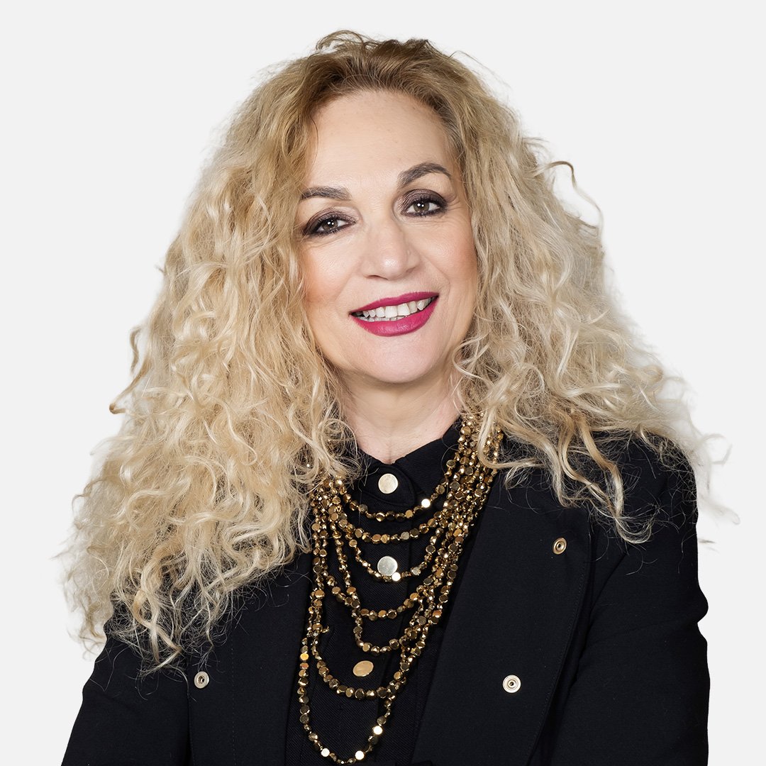 Donna con capelli biondi e ricci, indossa un completo nero, sfondo bianco.
