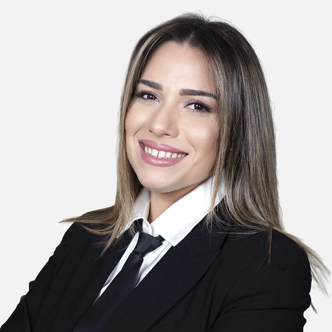 Donna con capelli castano chiaro, indossa una giacca nera, una camicia bianca e una cravatta nera, sfondo bianco
