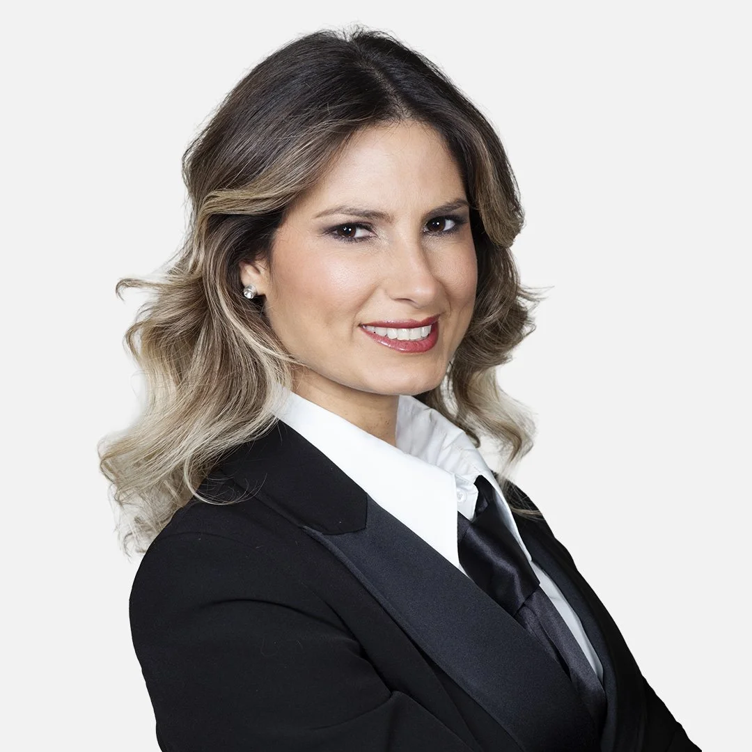 Donna sorridente, indossa una giacca nera, una camicia bianca e una cravatta nera, sfondo bianco