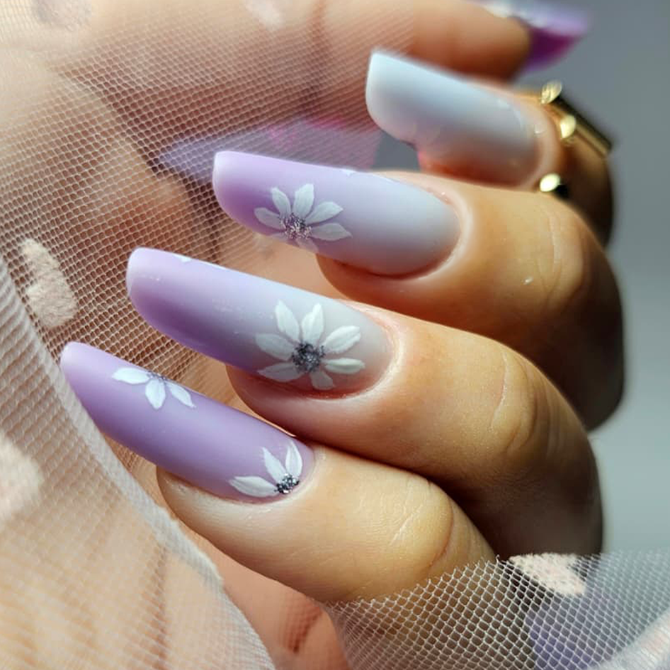 Manicure con unghie decorate con glitter e linee bianche su sfondo rosa chiaro.