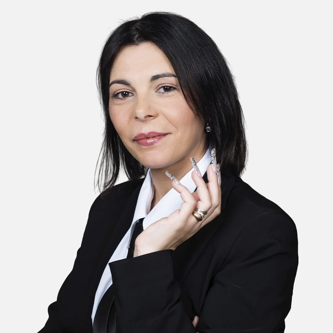 Donna con capelli scuri, indossa una giacca nera e una maglietta bianca, sfondo bianco.