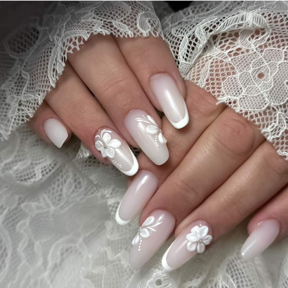Mano con unghie lunghe e smalto rosa chiaro, decorazioni floreali su due unghie.