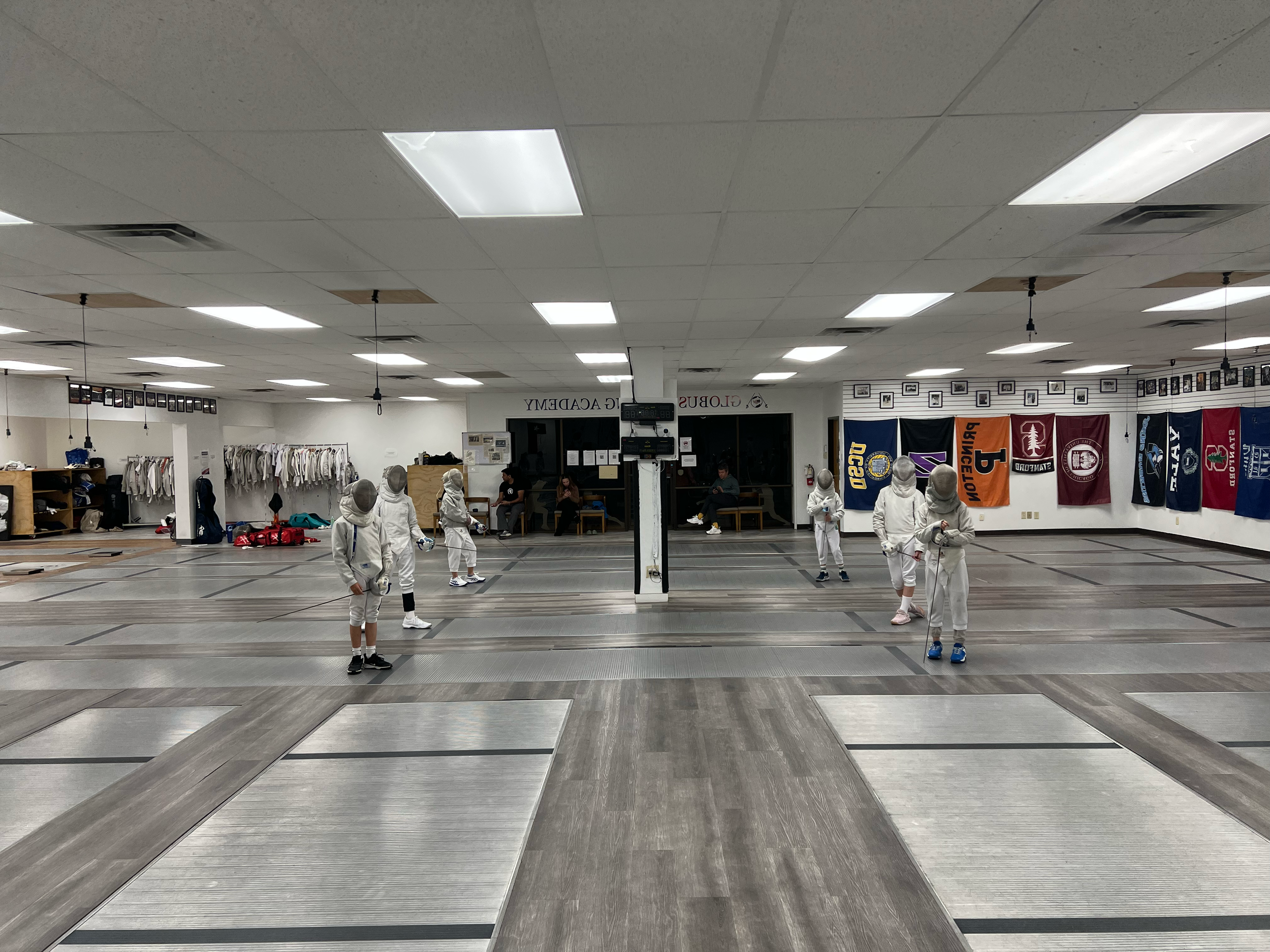 Fencing students wearing protective gear in a fencing gym.
