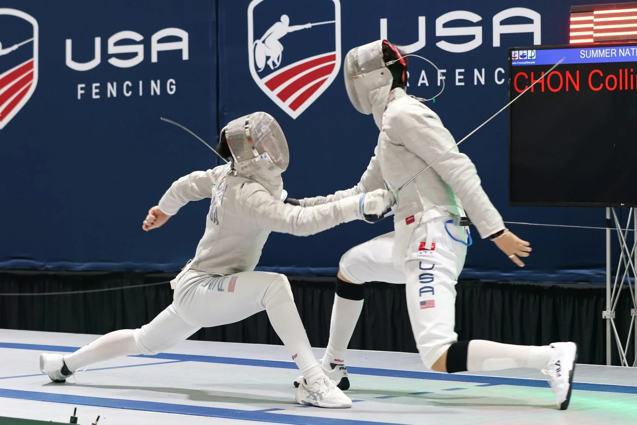 Two fencers in white protective gear engaged in a match, with one lunging towards the other.