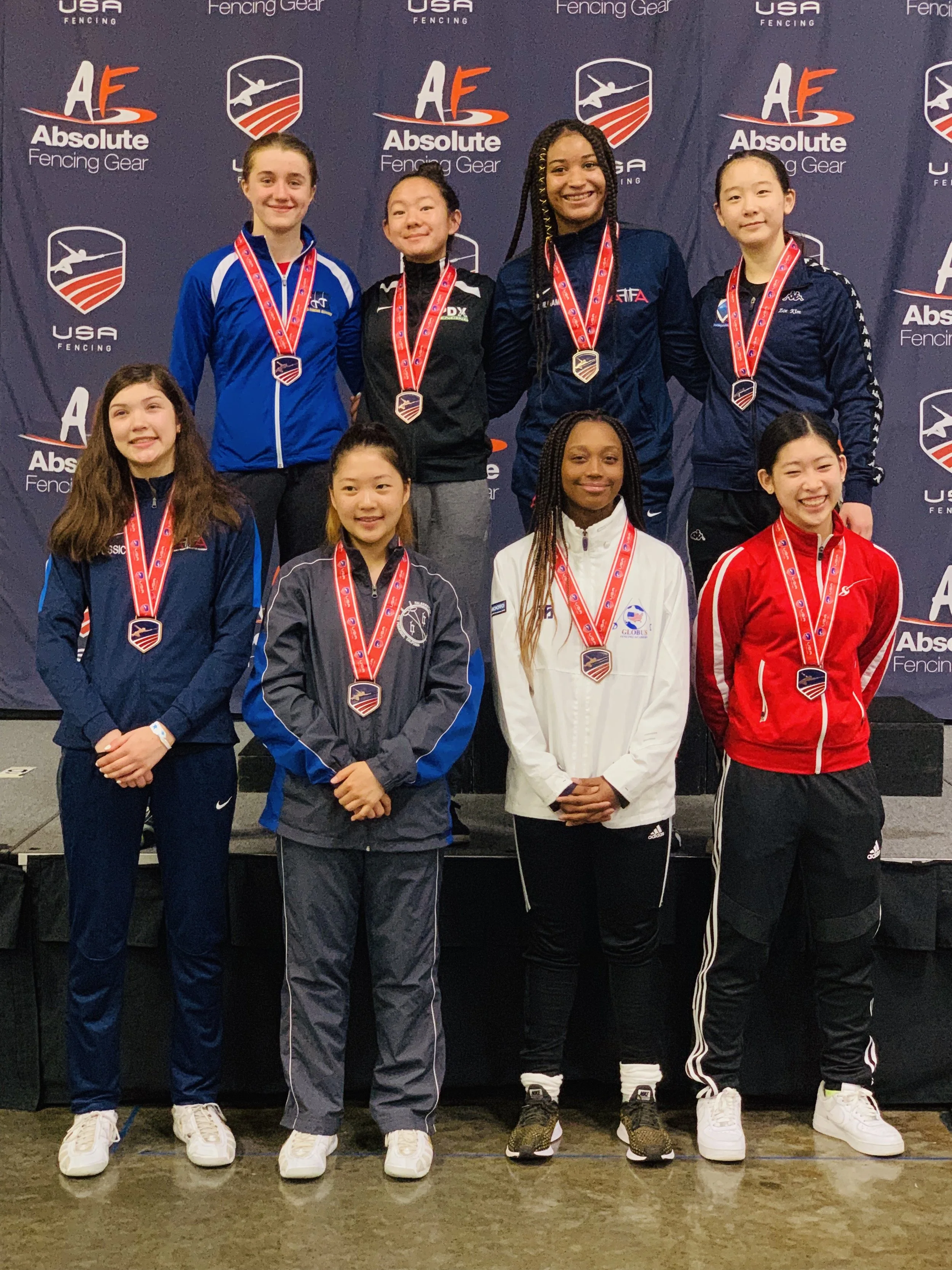 Young female athletes with medals posing on a podium at a fencing competition.