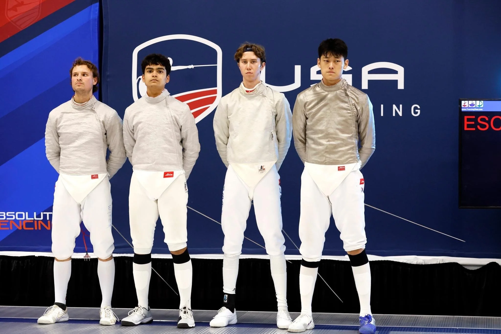 Four fencers stand side by side wearing fencing uniforms, in front of a dark blue background with a large logo.