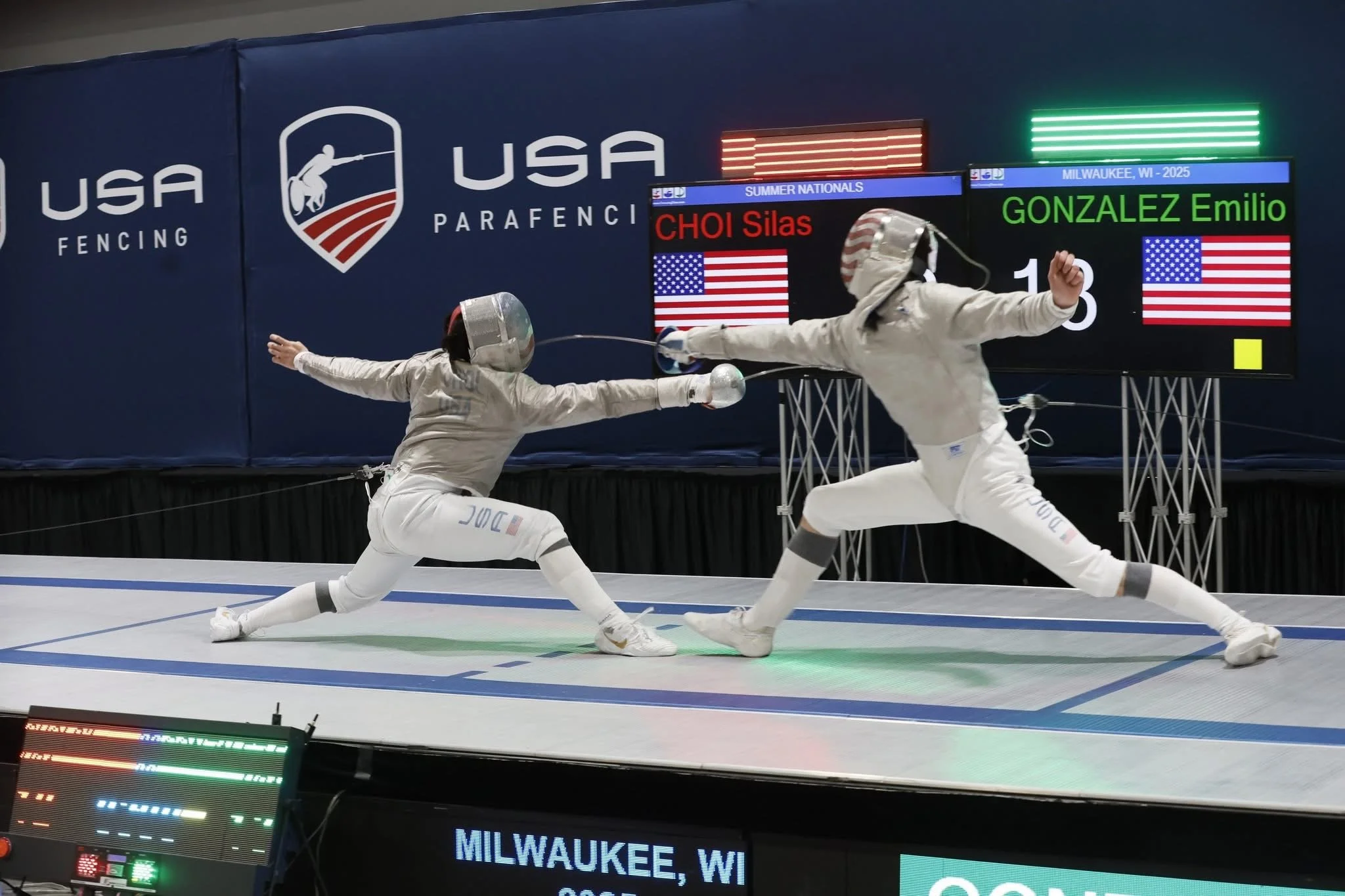 Two female fencers in full gear engage in a match, lunging toward each other with swords, on a fencing strip during a competition in Milwaukee, Wisconsin.